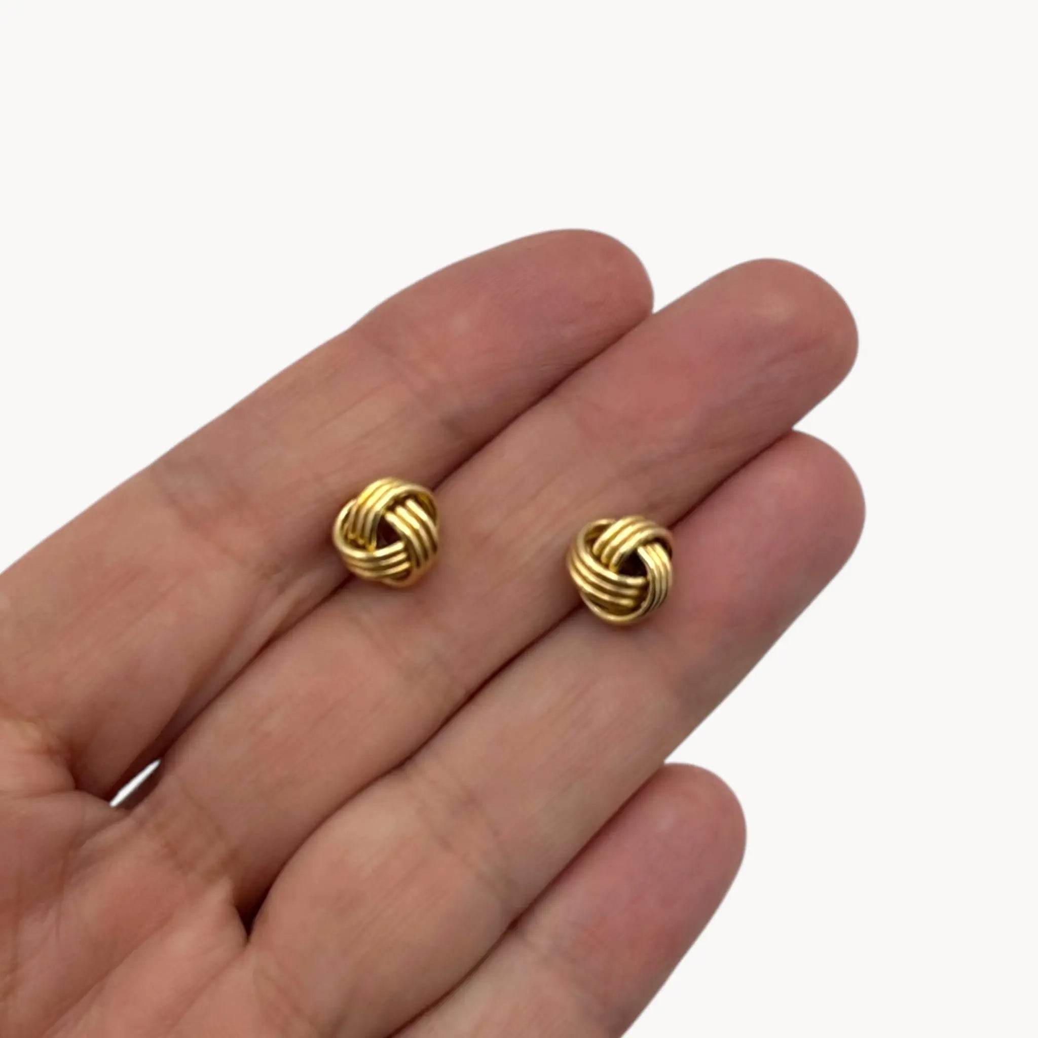 Displayed on hand for scale 10K yellow gold knot stud pierced earrings, classic love knot design on white background.