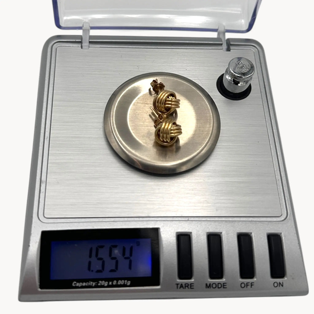 On scale view of 10K yellow gold knot stud pierced earrings, classic love knot design on white background.