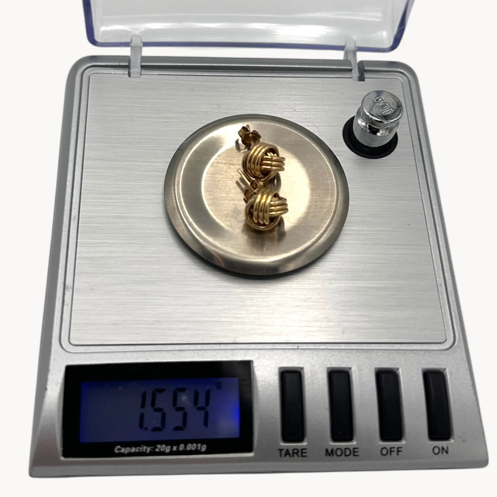 On scale view of 10K yellow gold knot stud pierced earrings, classic love knot design on white background.