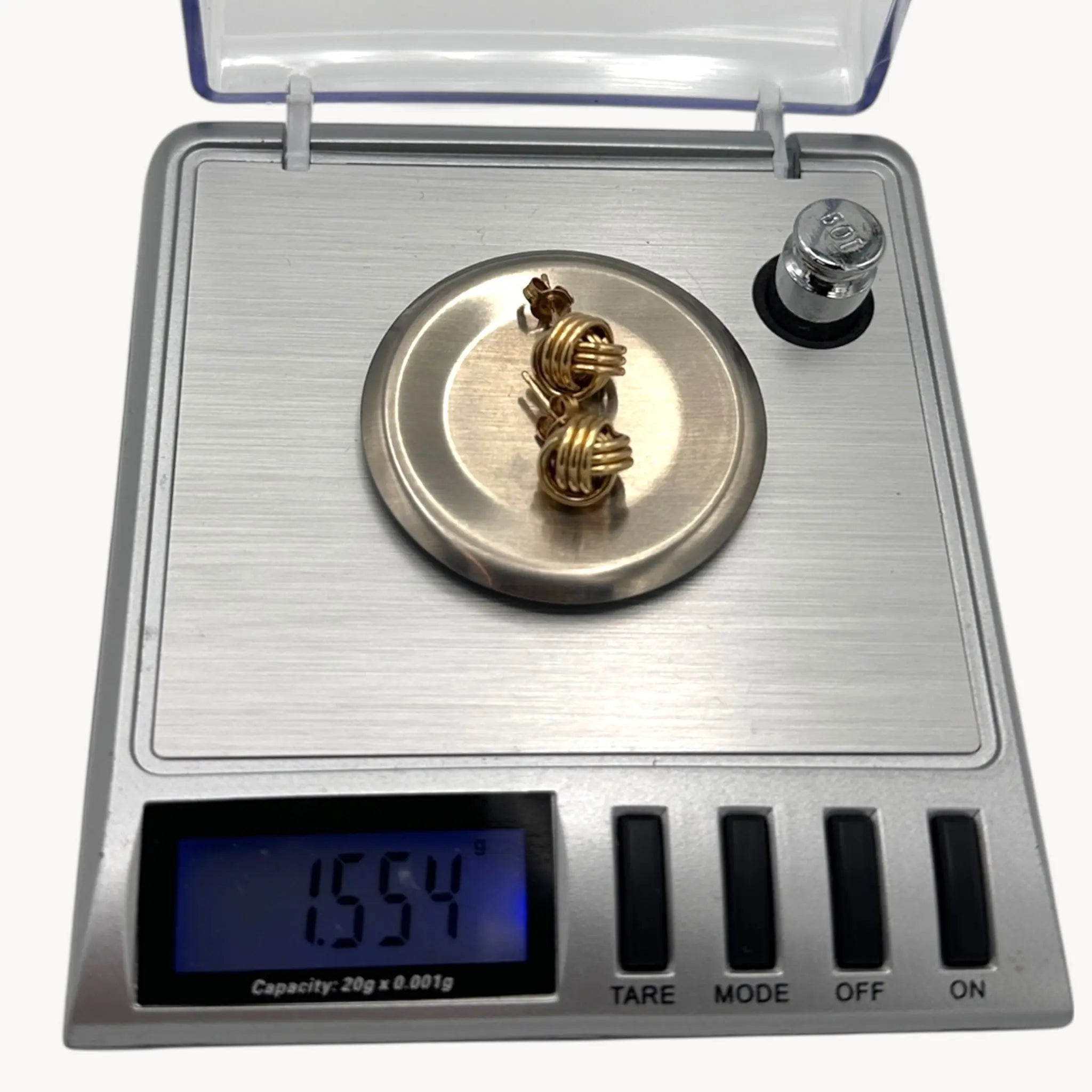 On scale view of 10K yellow gold knot stud pierced earrings, classic love knot design on white background.