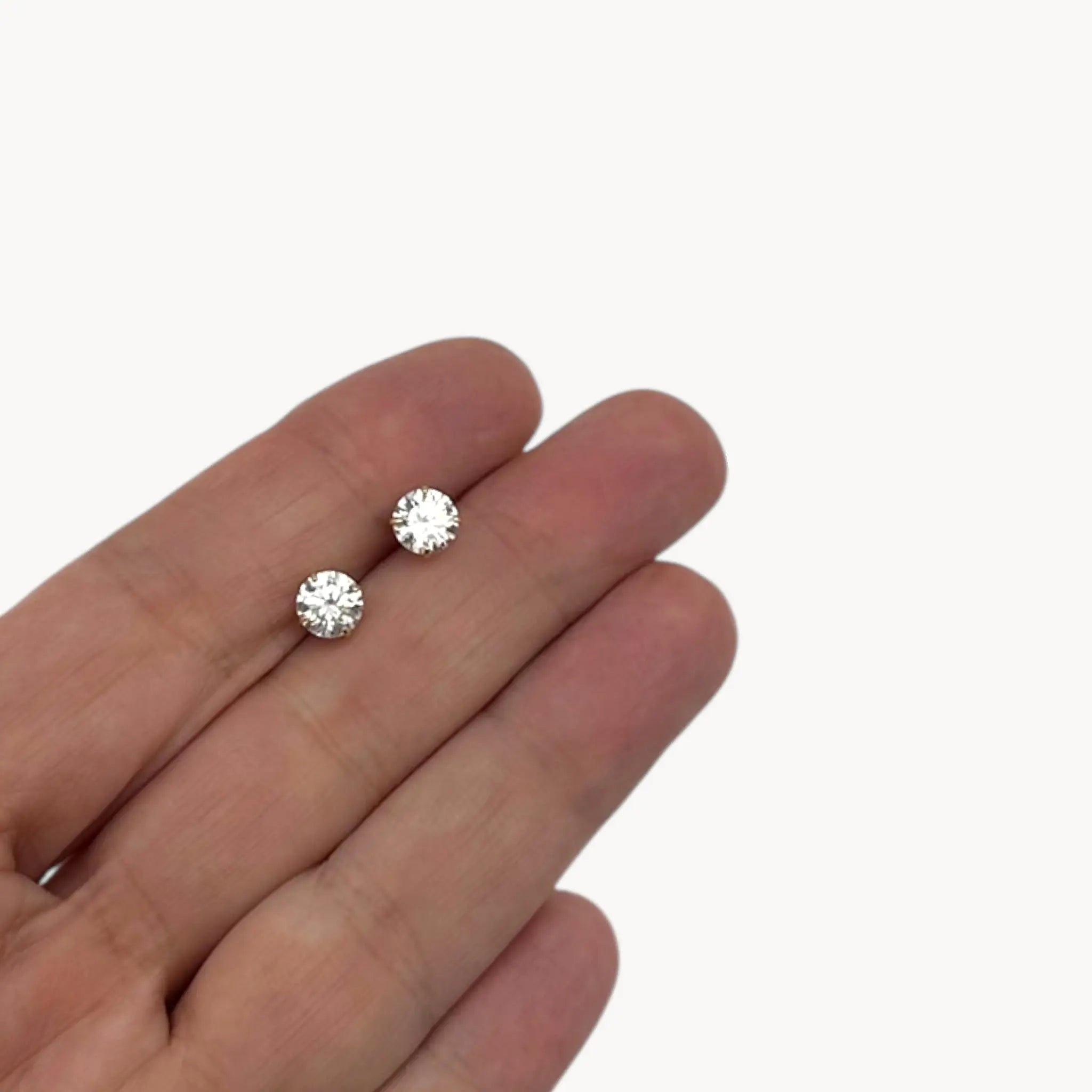 Displayed on hand 14K yellow gold cubic zirconia solitaire stud earrings displayed on white background.