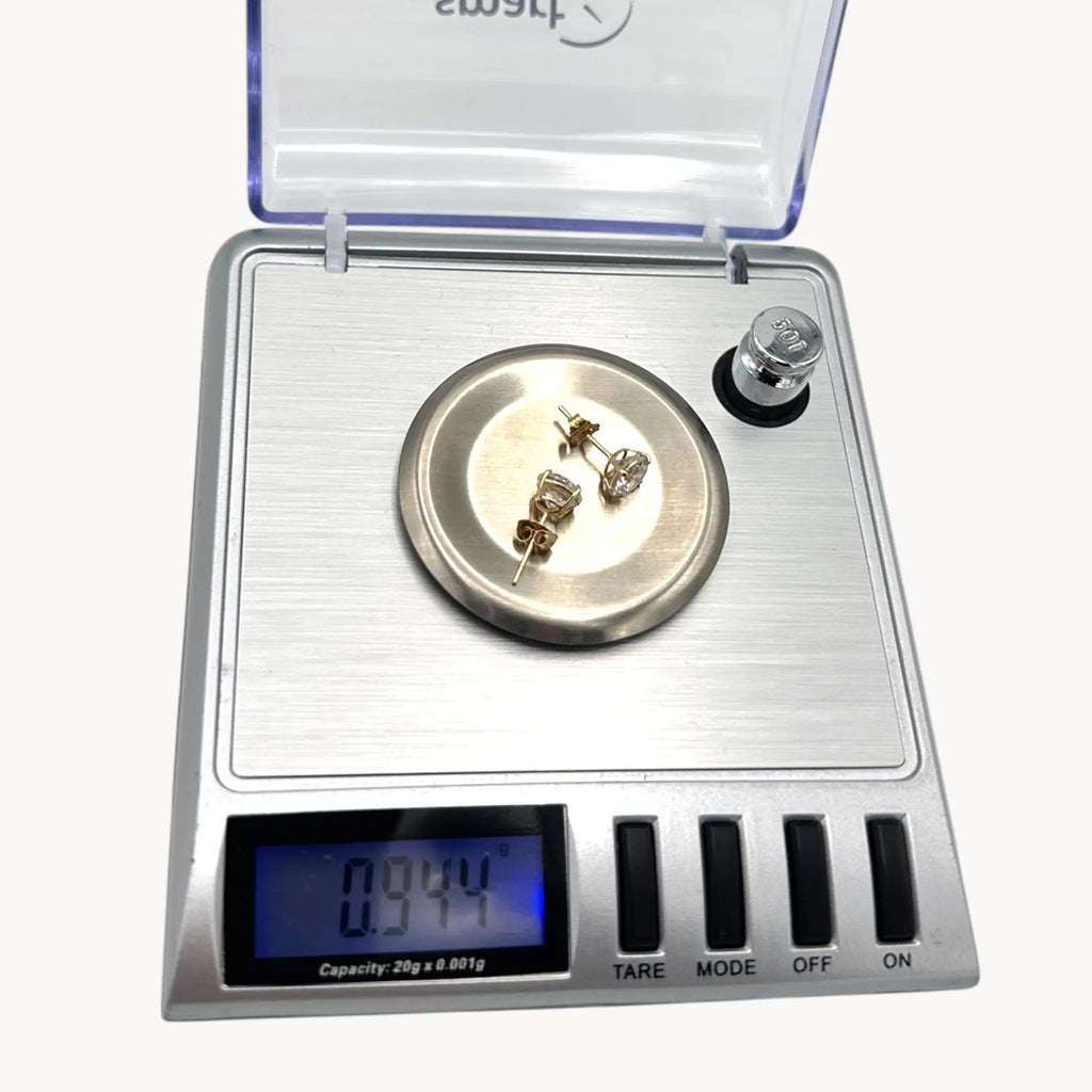 On scale view of 14K yellow gold cubic zirconia solitaire stud earrings displayed on white background.