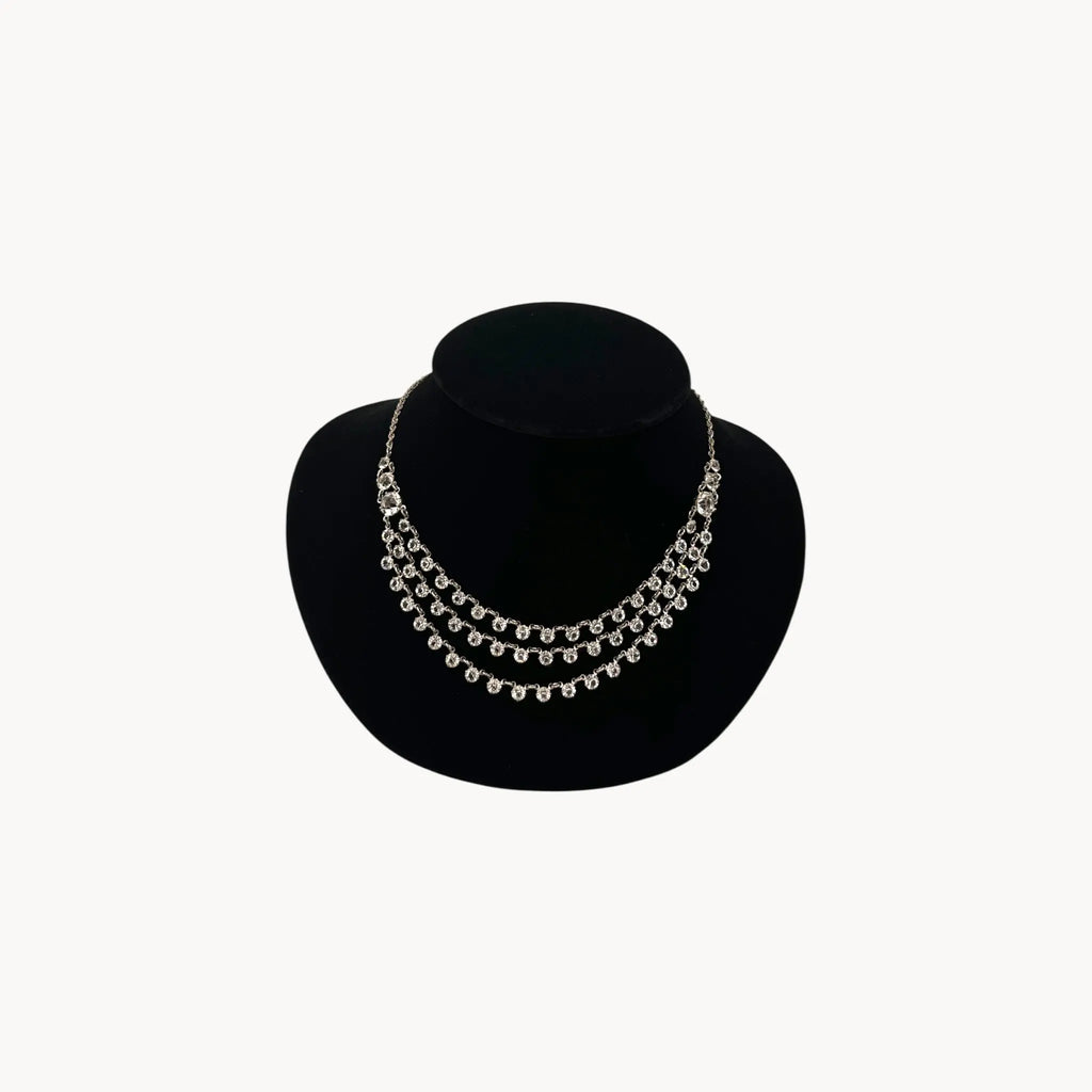 Art Deco style rhodium plated three-row crystal draped necklace on black bust.