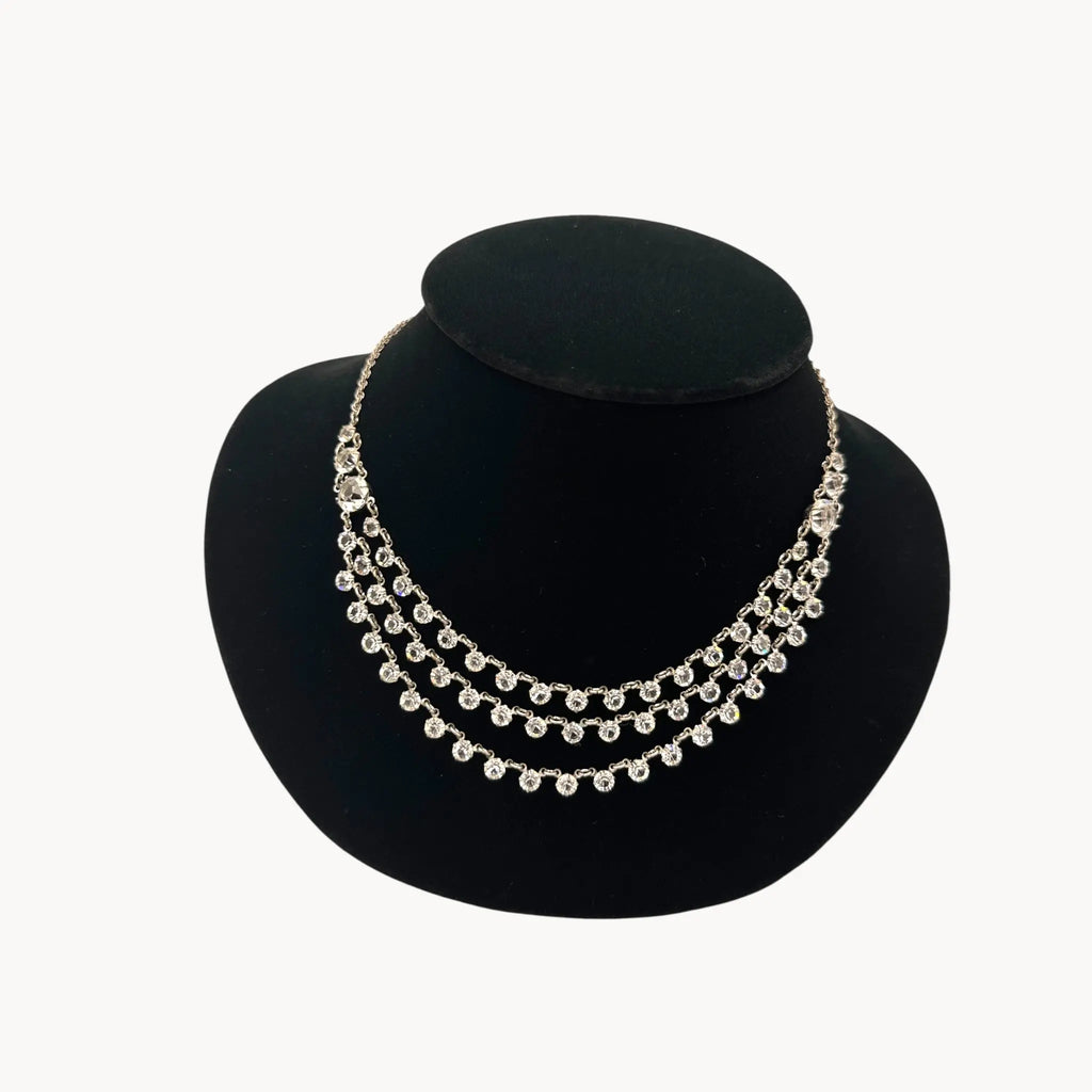 Close up view of Art Deco style rhodium plated three-row crystal draped necklace on black bust.