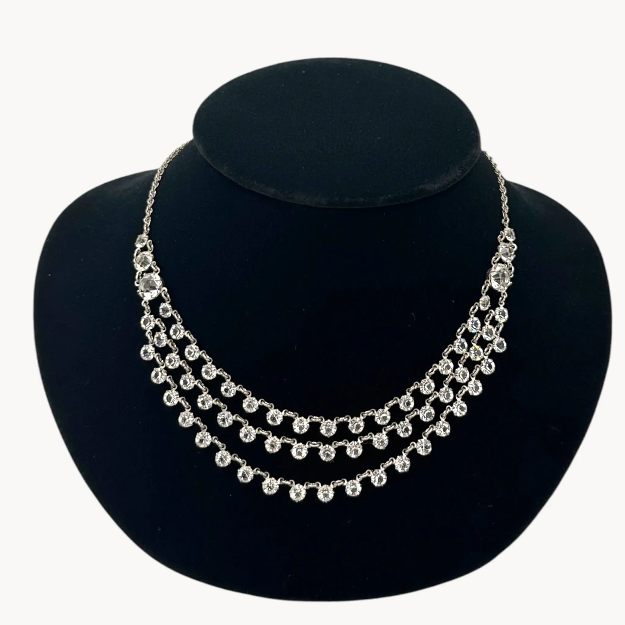 Close up view of Art Deco style rhodium plated three-row crystal draped necklace on black bust.