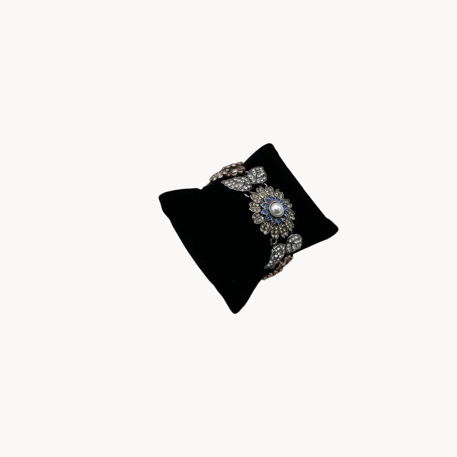Side view of Chloe + Isabel multi-color floral rhinestone bracelet with pearls and crystal leaves on black pillow and white background. 