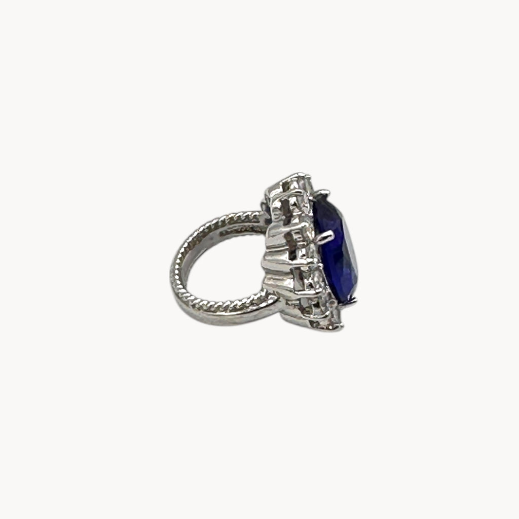 Side view of Kenneth Jay Lane blue oval crystal cocktail ring inspired by Princess Diana’s sapphire engagement ring on white background.