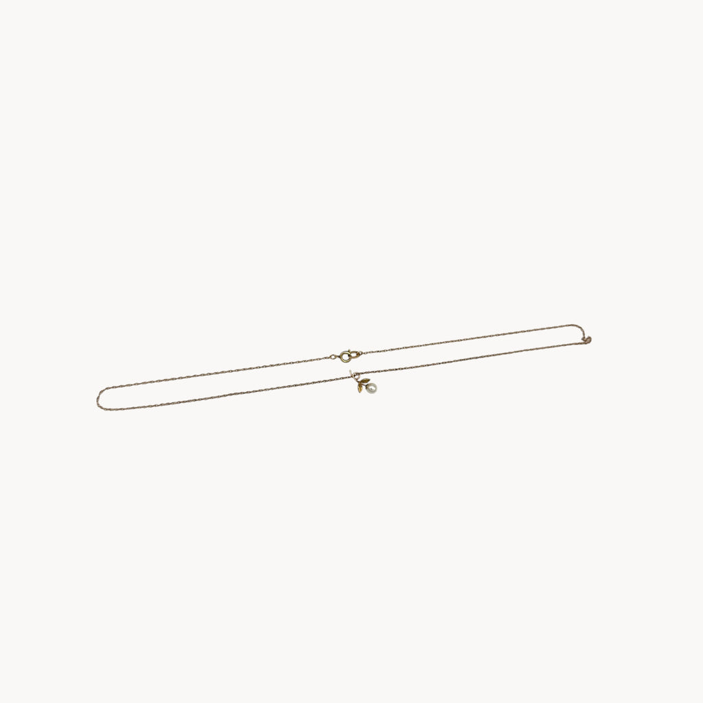 Flat lay on white background of Krementz dainty gold flower pendant necklace with pearl center.