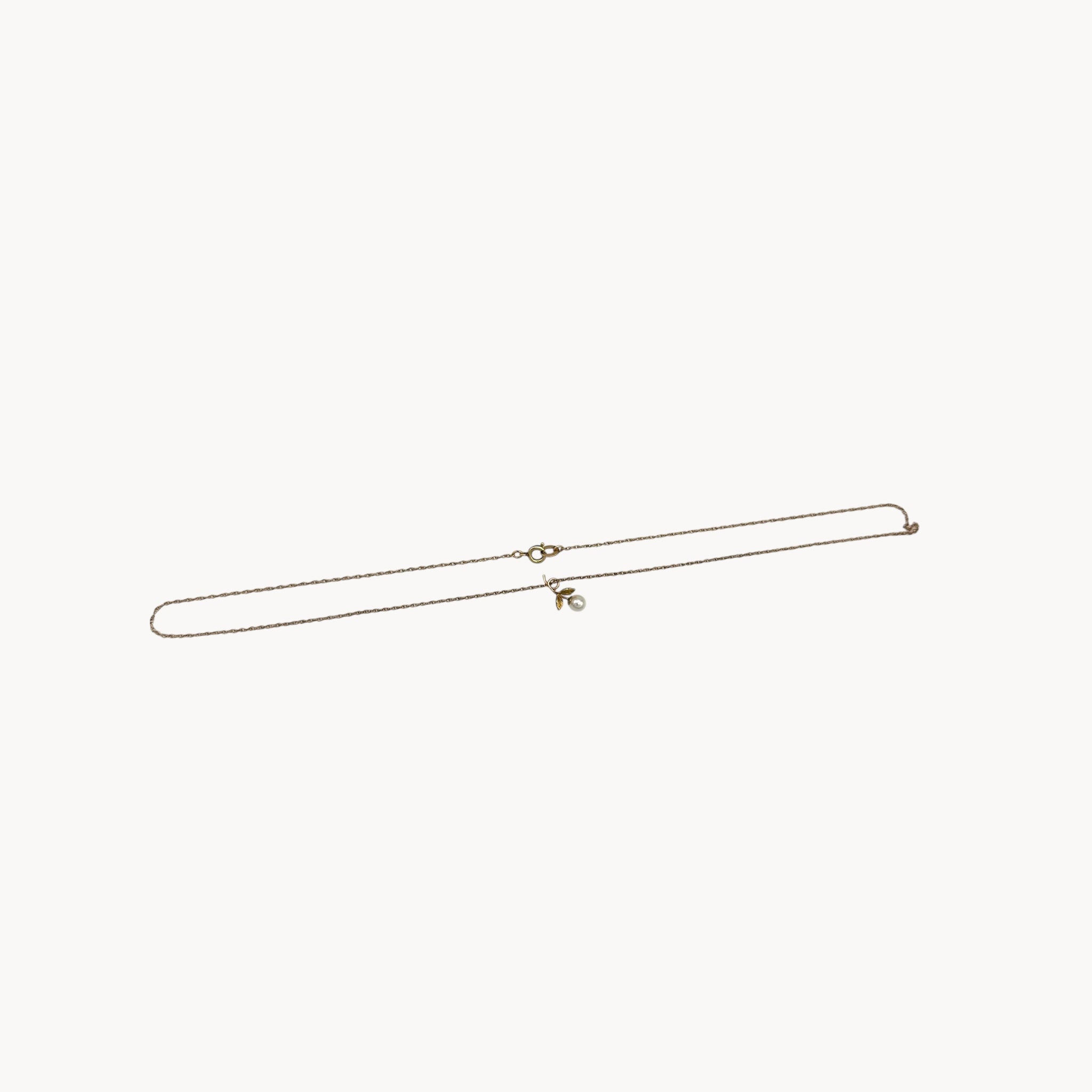 Flat lay on white background of Krementz dainty gold flower pendant necklace with pearl center.