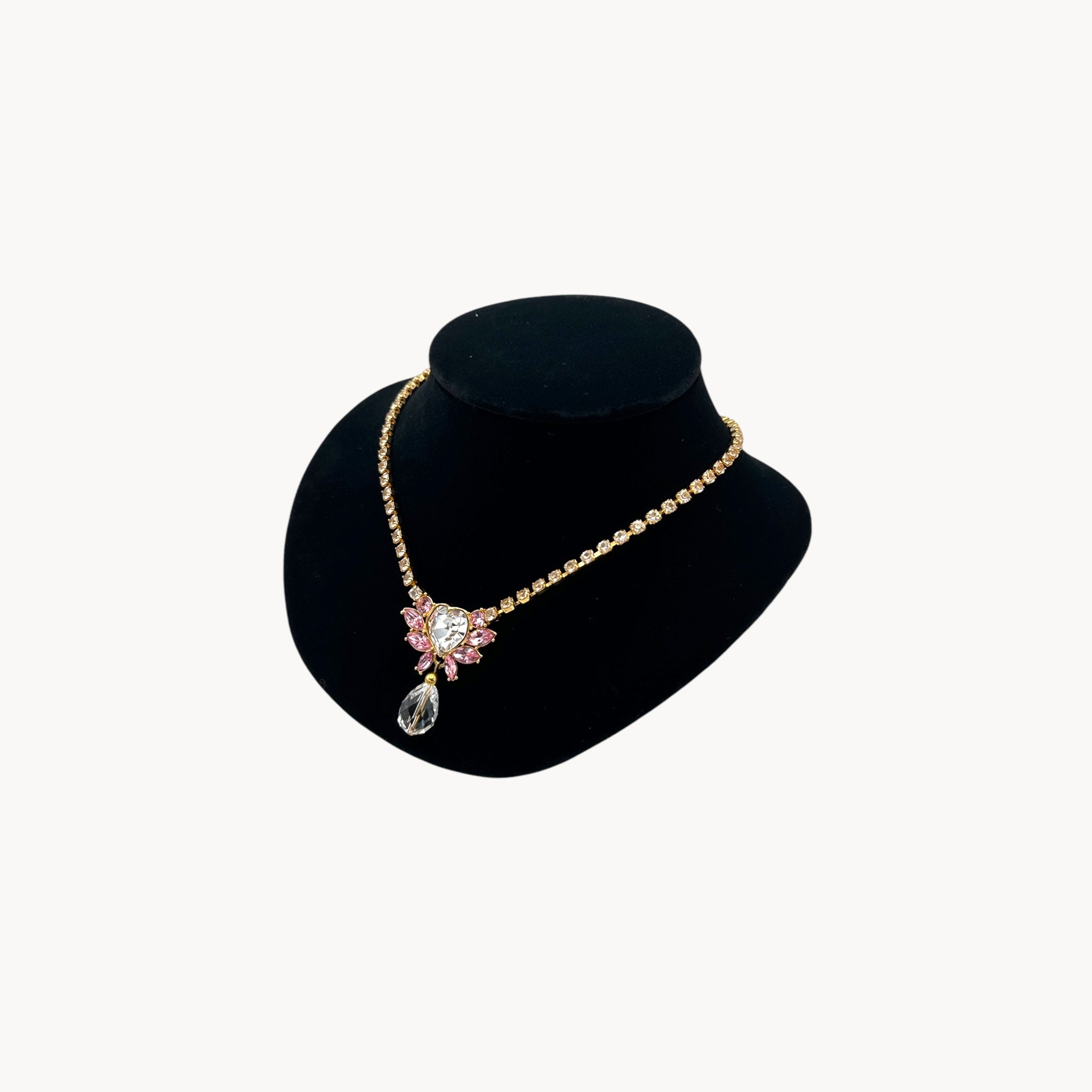 Side view of pendant of Vintage Monet gold necklace and clip-on earring set with clear heart and pink rhinestones.