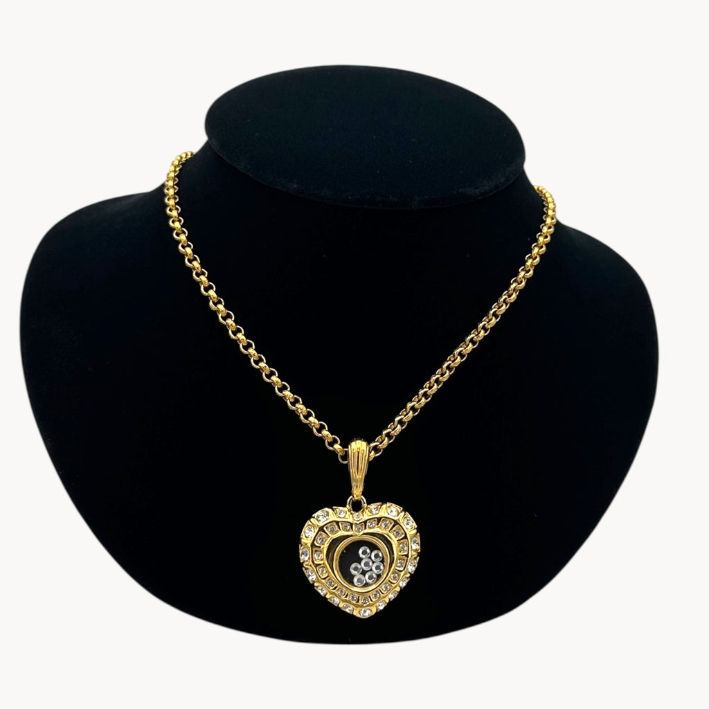 Close up view of Nolan Miller gold-tone heart pendant necklace with clear rhinestones on long chain on black bust.
