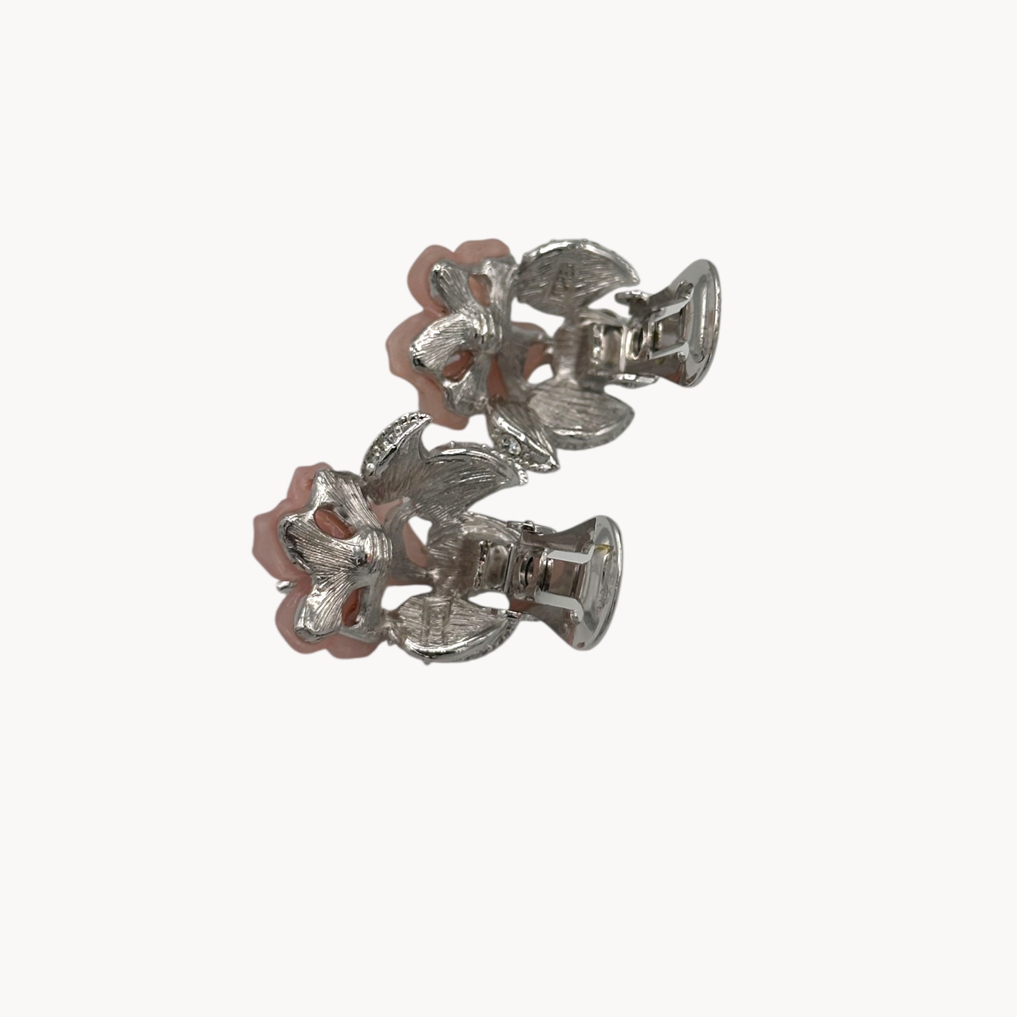 Back view with clips open of Nolan Miller vintage pink flower clip-on earrings with rhinestone accents and silver-tone leaves