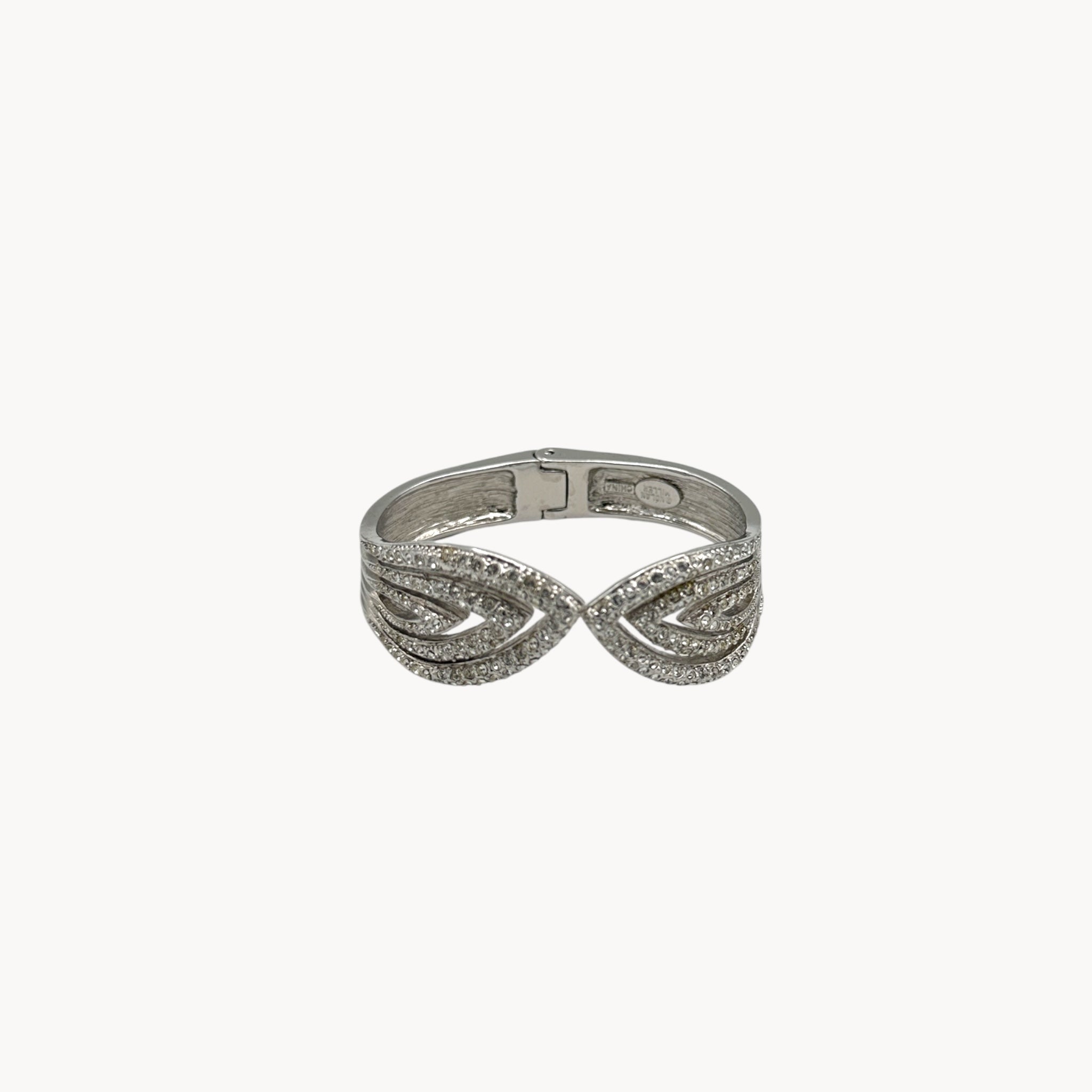 View against white of Nolan Miller silver rhinestone hinged bangle bracelet with overlapping design.