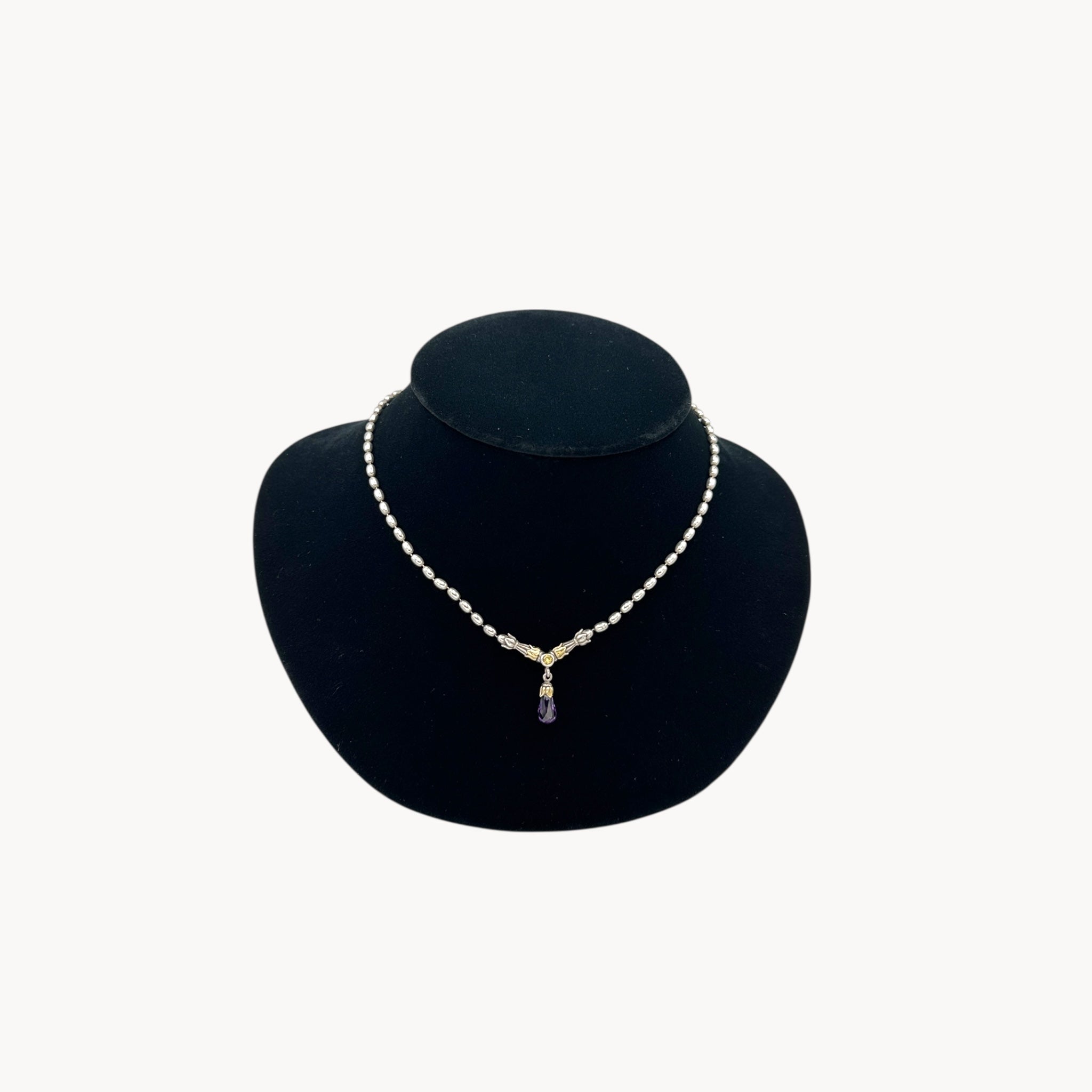 Sterling silver and 14K yellow gold necklace with amethyst teardrop pendant on black bust.