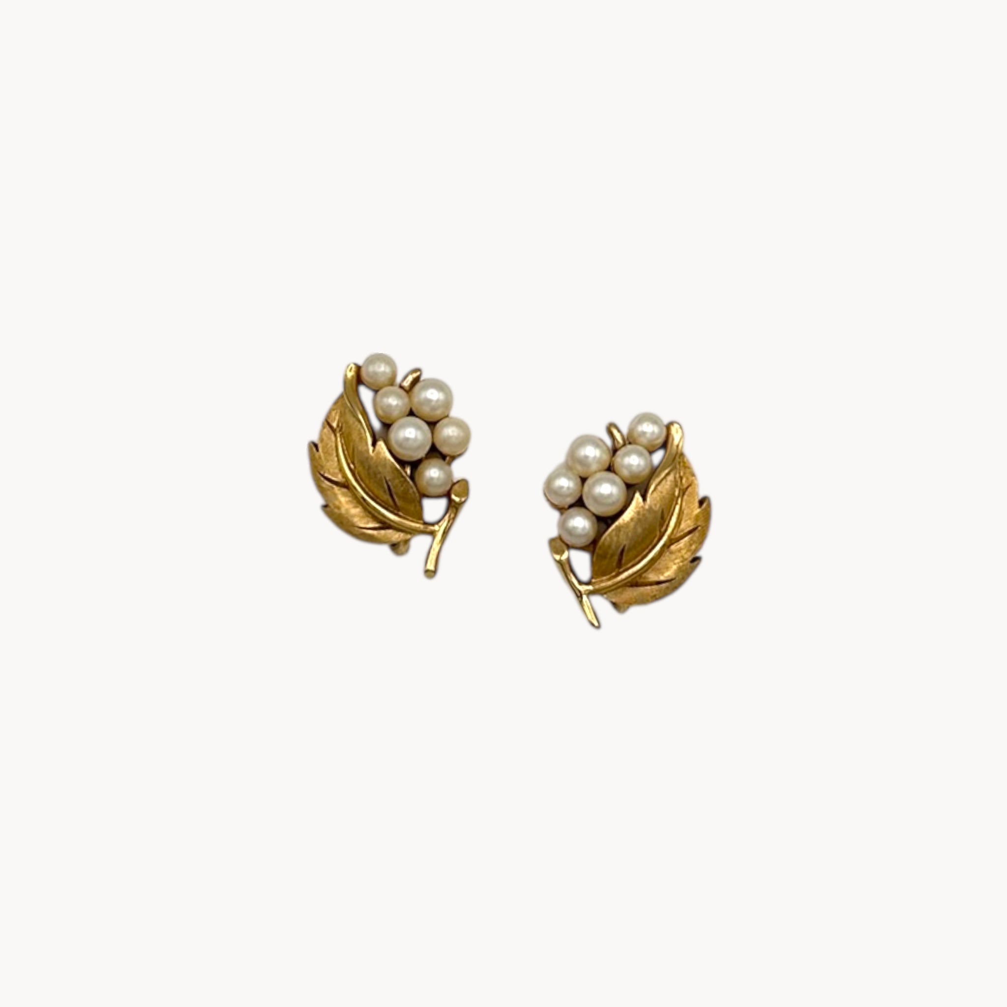 Vintage Trifari gold leaf clip-on earrings with faux pearl clusters, mid-century jewelry on white back background.