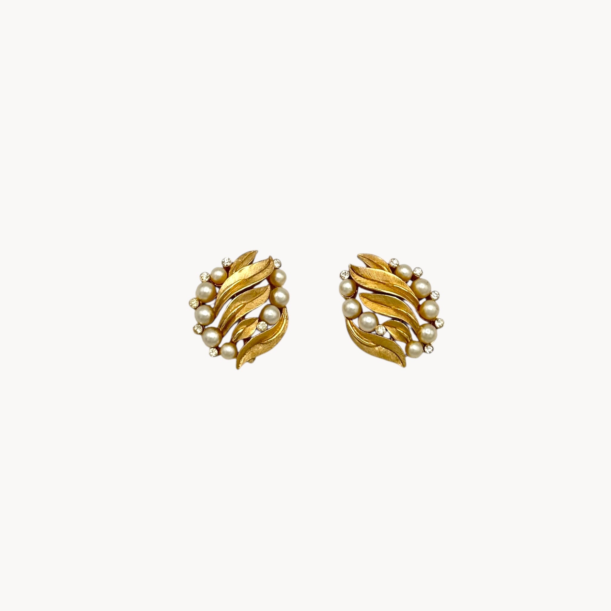 Vintage Trifari gold floral clip-on earrings with faux pearls and rhinestones, 1960s jewelry on white background.