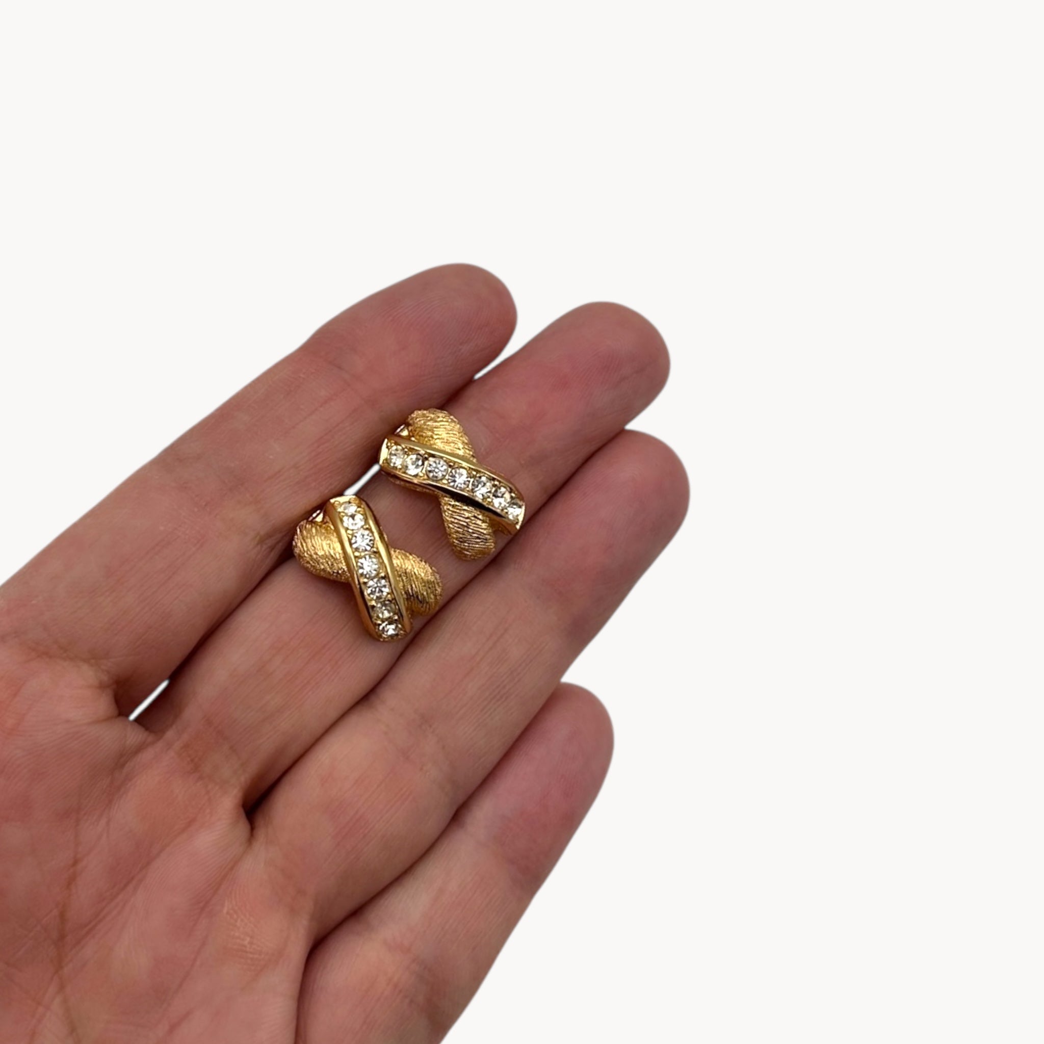Scale size view of Vintage Christian Dior petite gold-tone clip-on earrings with rhinestone ribbon detail.