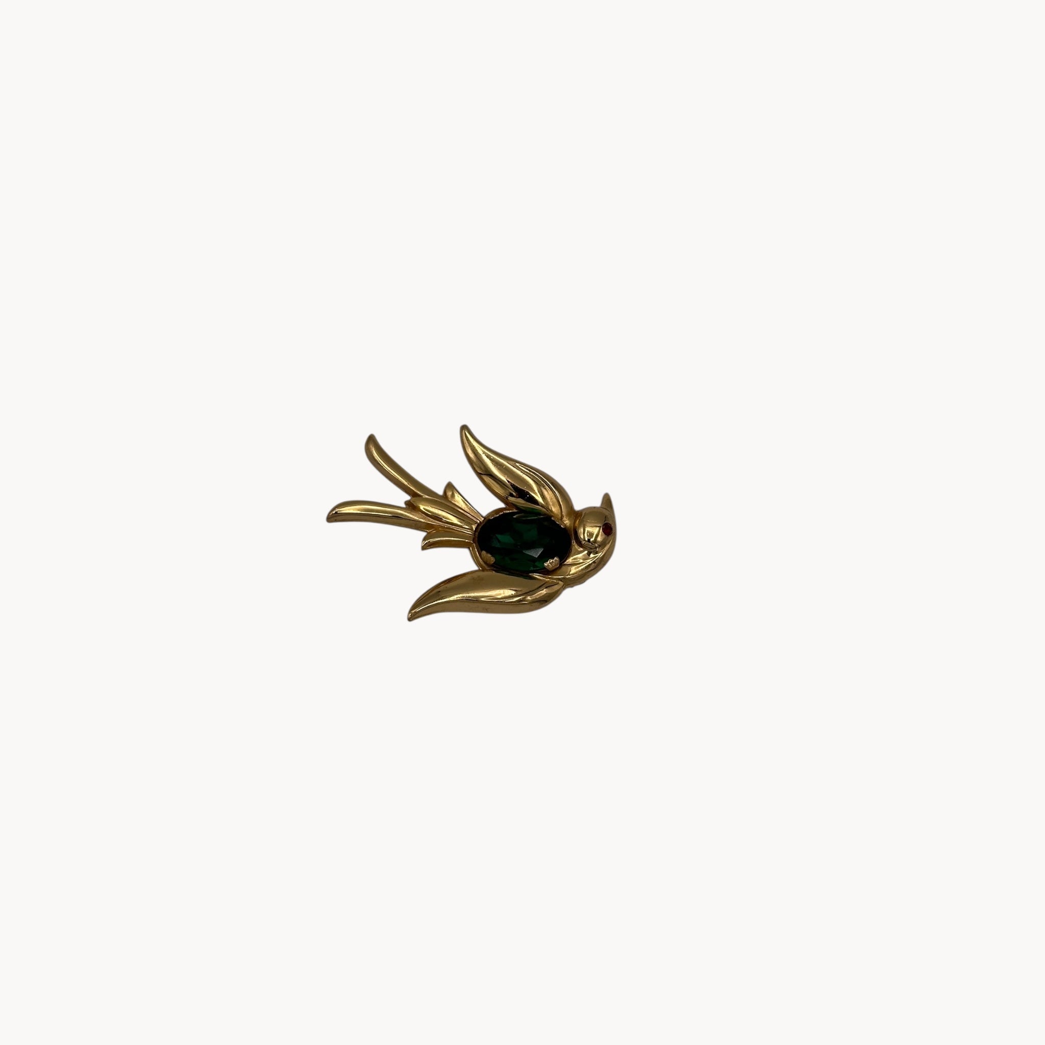 Close up view Vintage Coro gold-tone bird brooch with green glass stone body and red eye accent, 1950s whimsical bridal accessory.