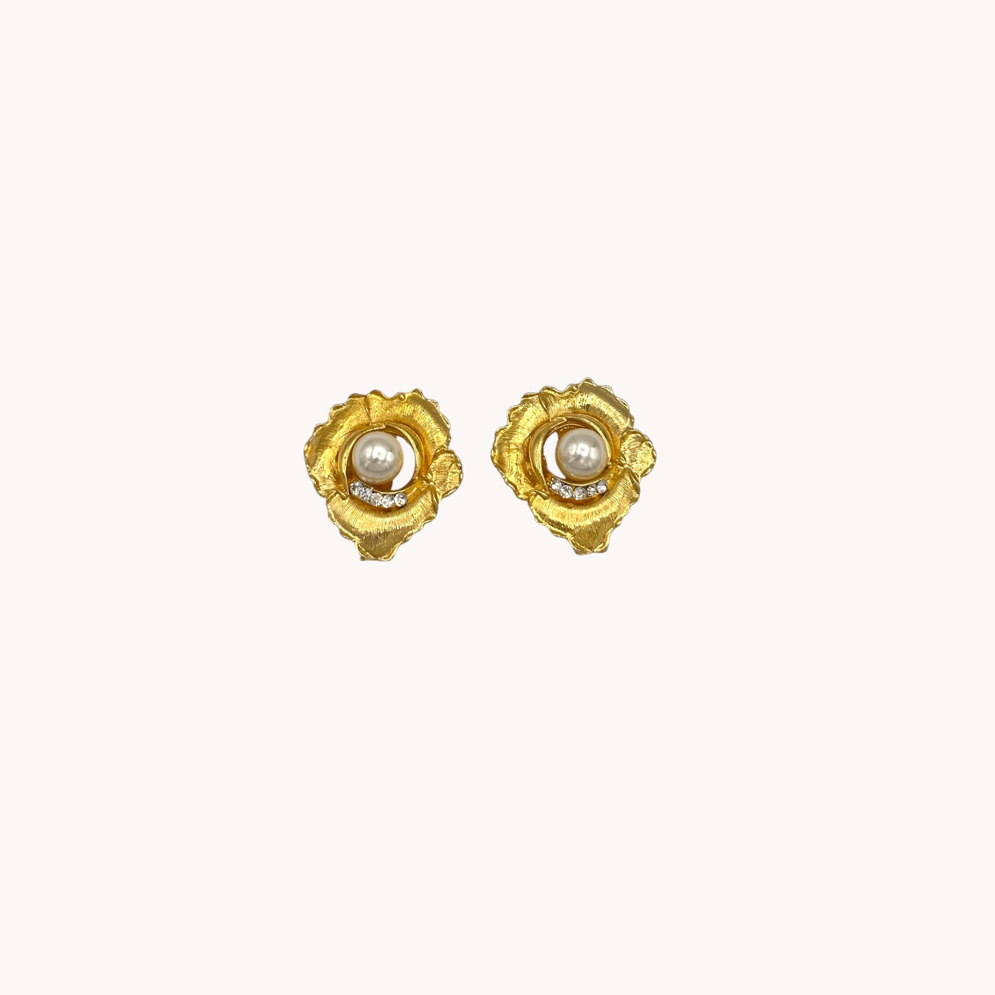 Close up picture of Vintage unmarked clip-on earrings with textured gold-tone floral design, faux pearl center, and crystal accents, 1980s bridal jewelry.