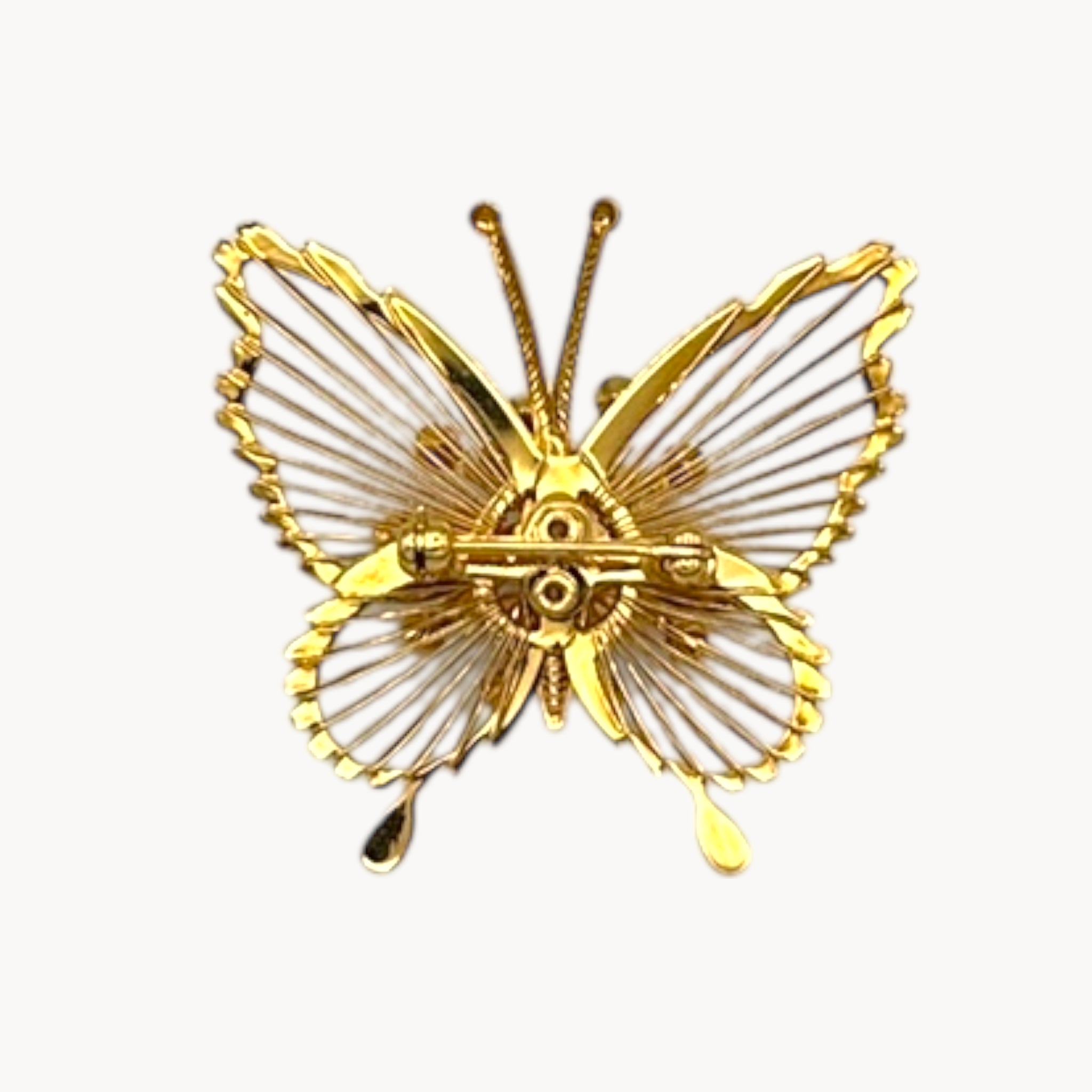 Back view of Vintage Monet butterfly brooch with gold openwork wings and faux pearl accents on white background.