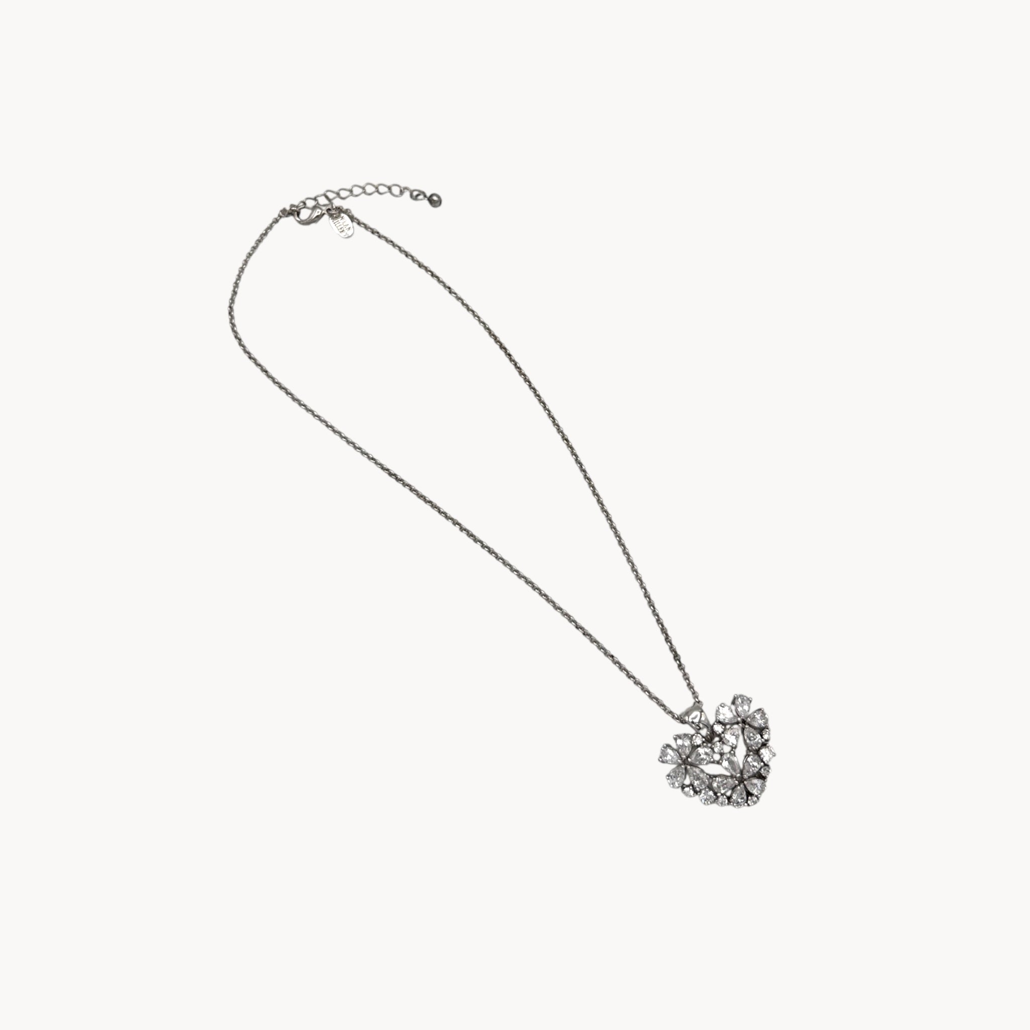 Vintage Nolan Miller rhinestone heart pendant necklace on silver chain on white background.