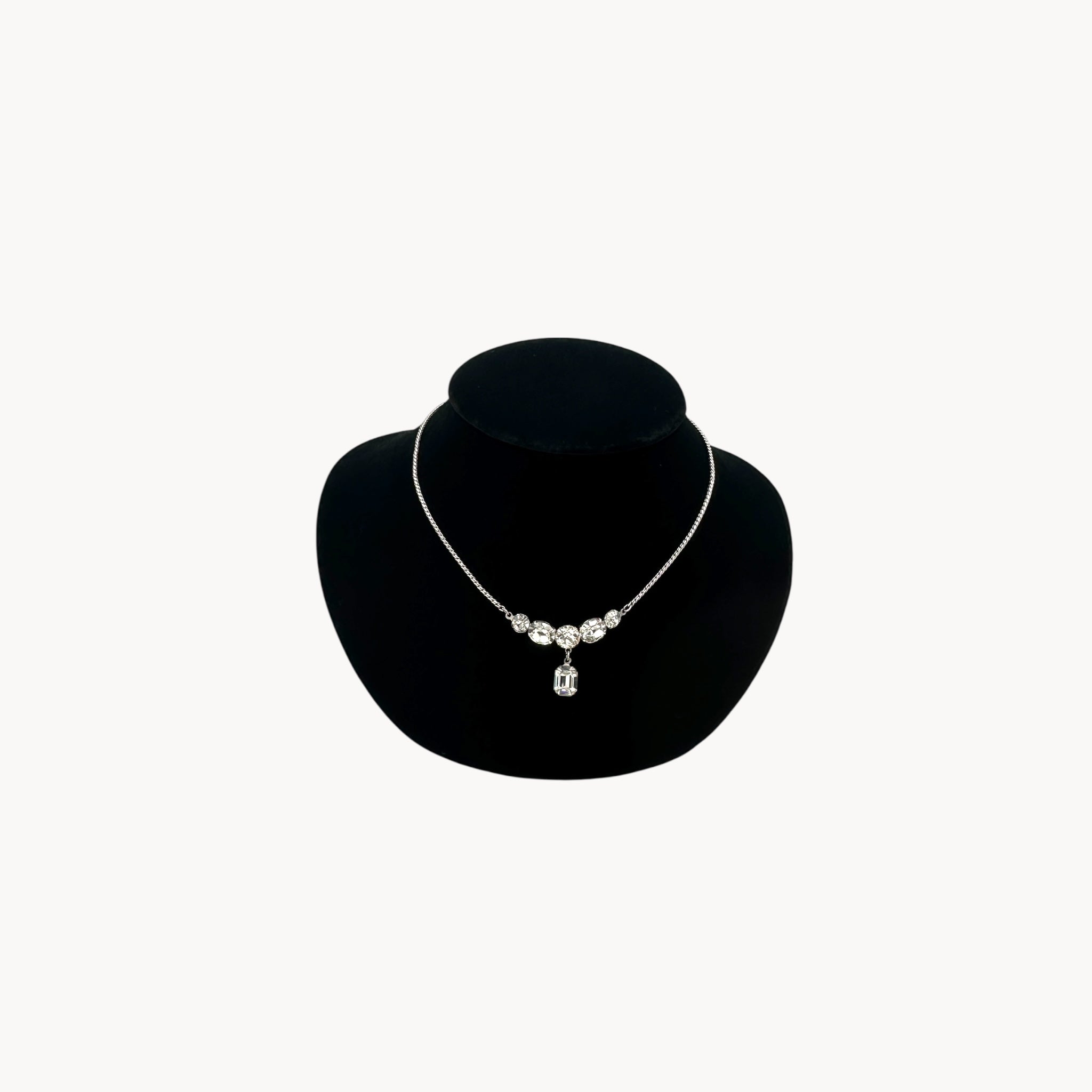 Vintage rhinestone pendant necklace with round and emerald-cut stones on black bust.