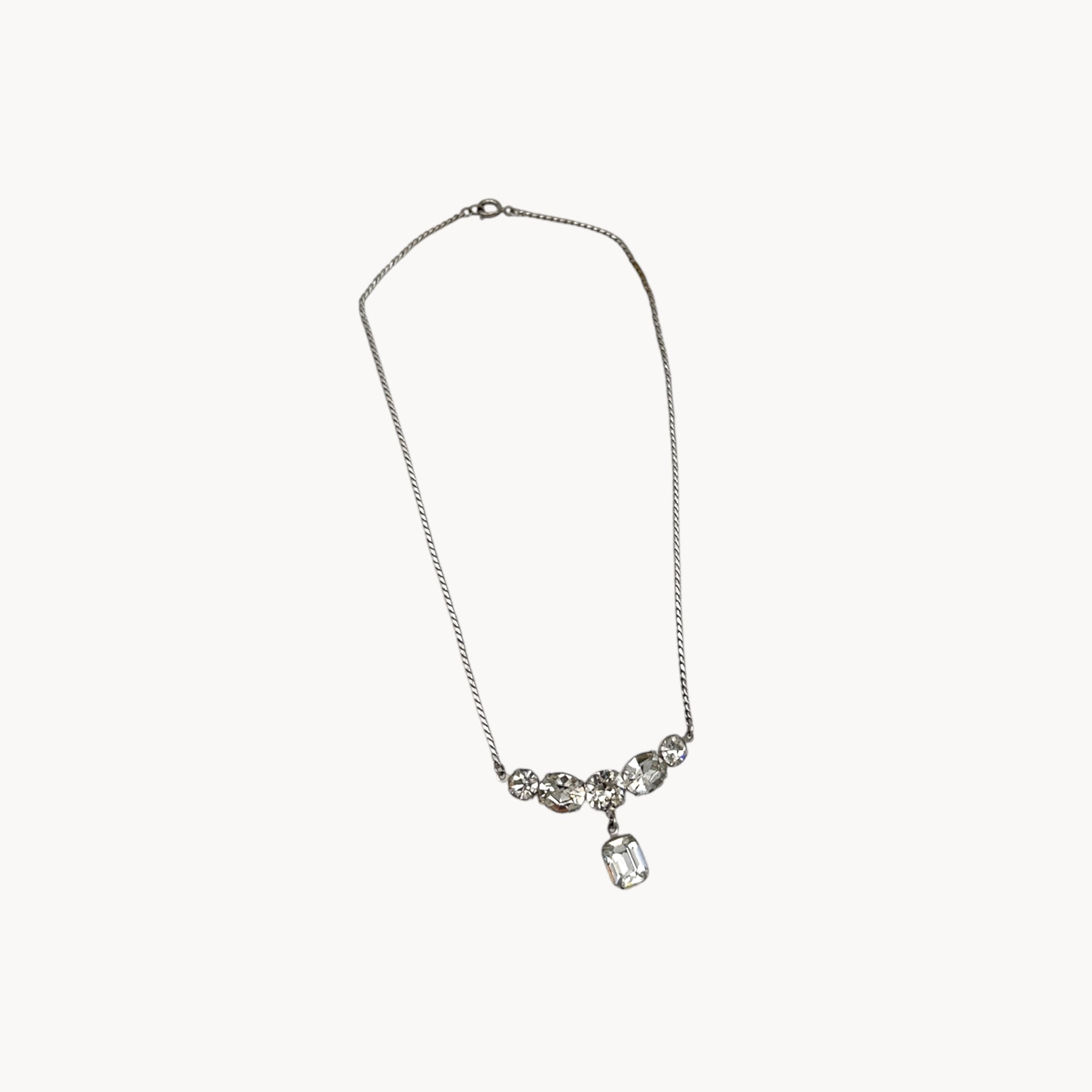 Vintage rhinestone pendant necklace with round and emerald-cut stones on white background.