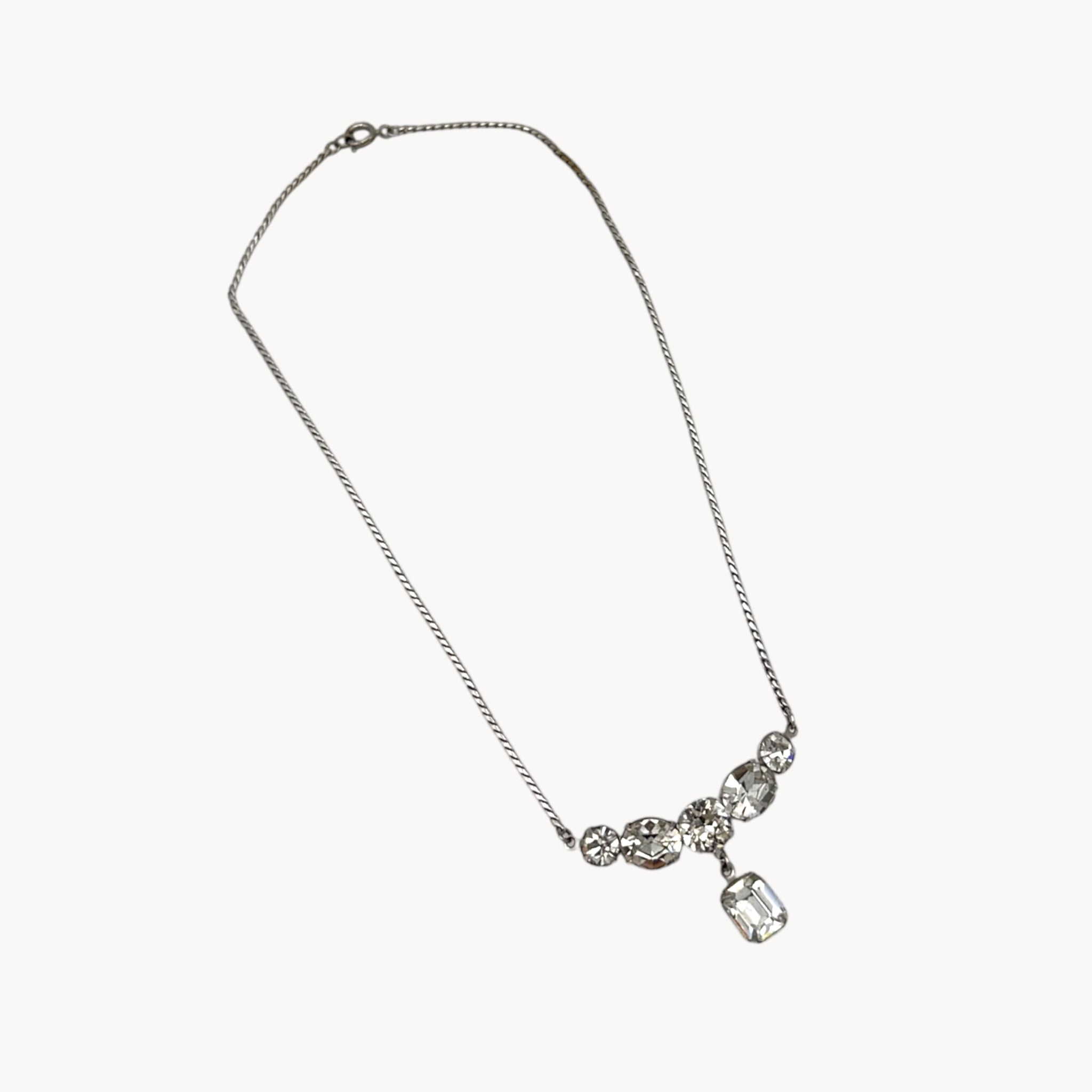 Close up view of Vintage rhinestone pendant necklace with round and emerald-cut stones on white background.