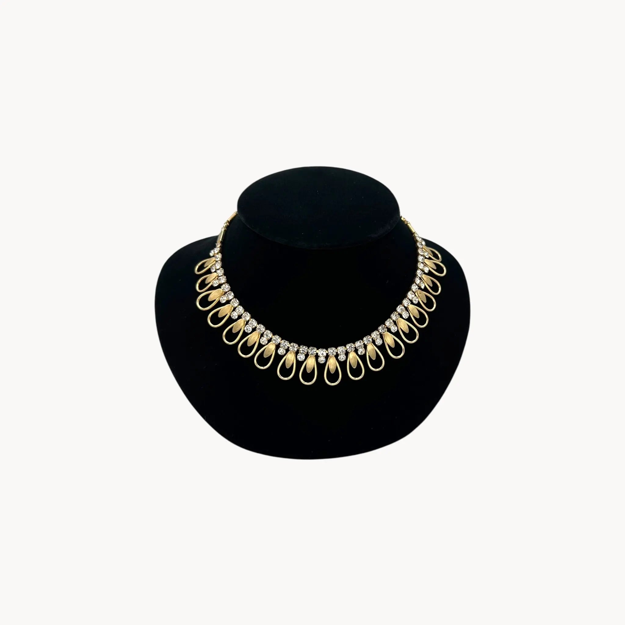 Vintage Sarah Coventry gold-tone teardrop bib necklace with clear rhinestones displayed on black velvet bust.