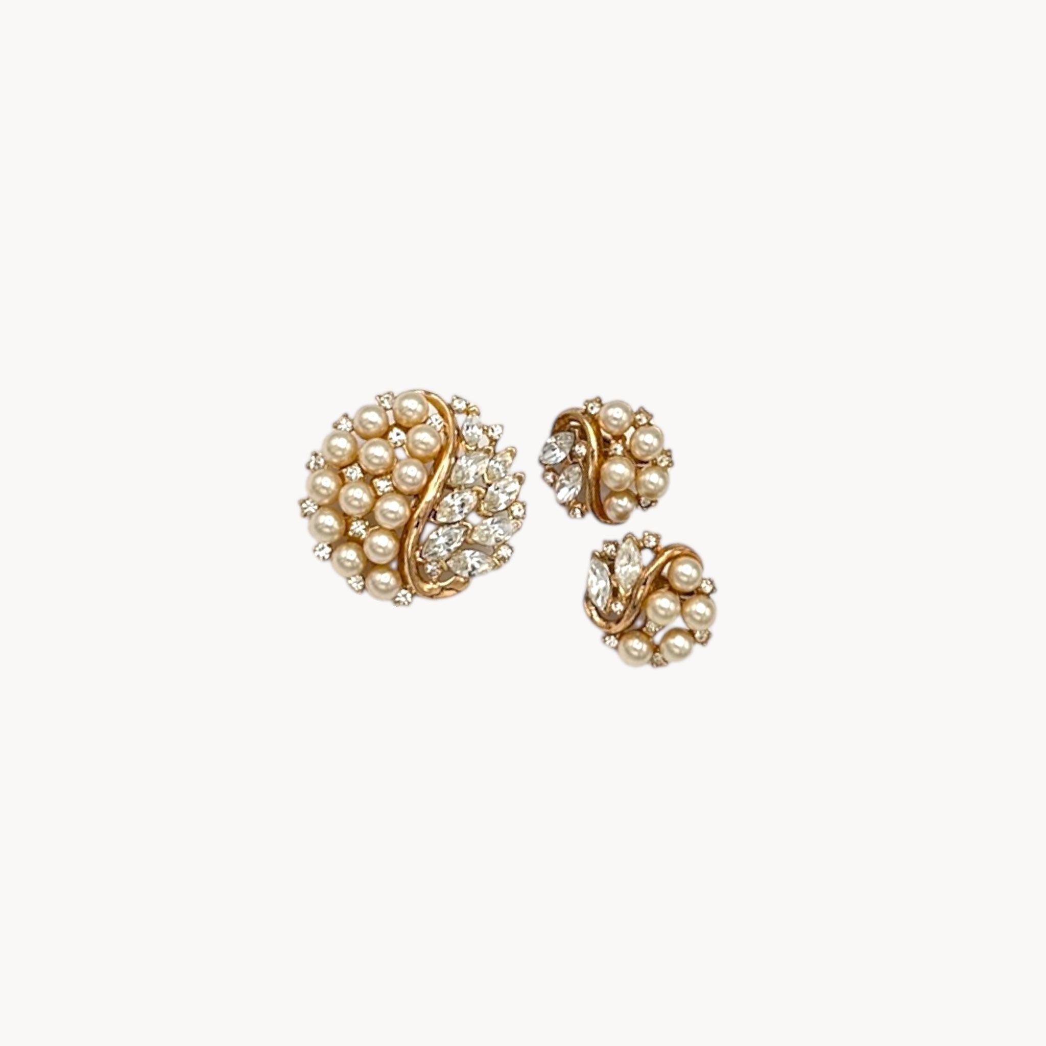 Vintage Trifari jewelry set with faux pearls, rhinestones, and gold-tone design including brooch and matching clip-on earrings shown on white background.