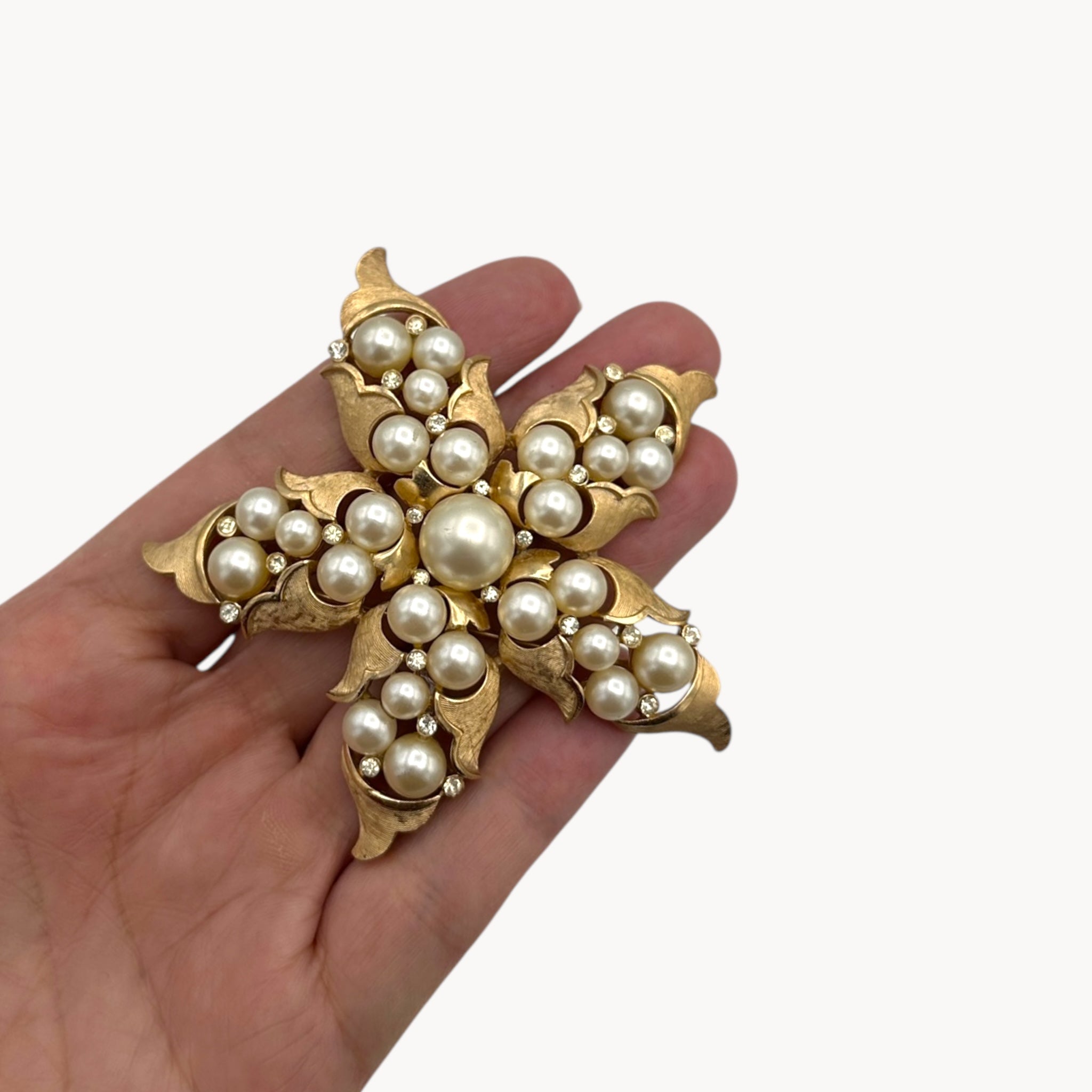 Scale view of Vintage Trifari floral starfish brooch with faux pearls and rhinestones in gold-tone metal.