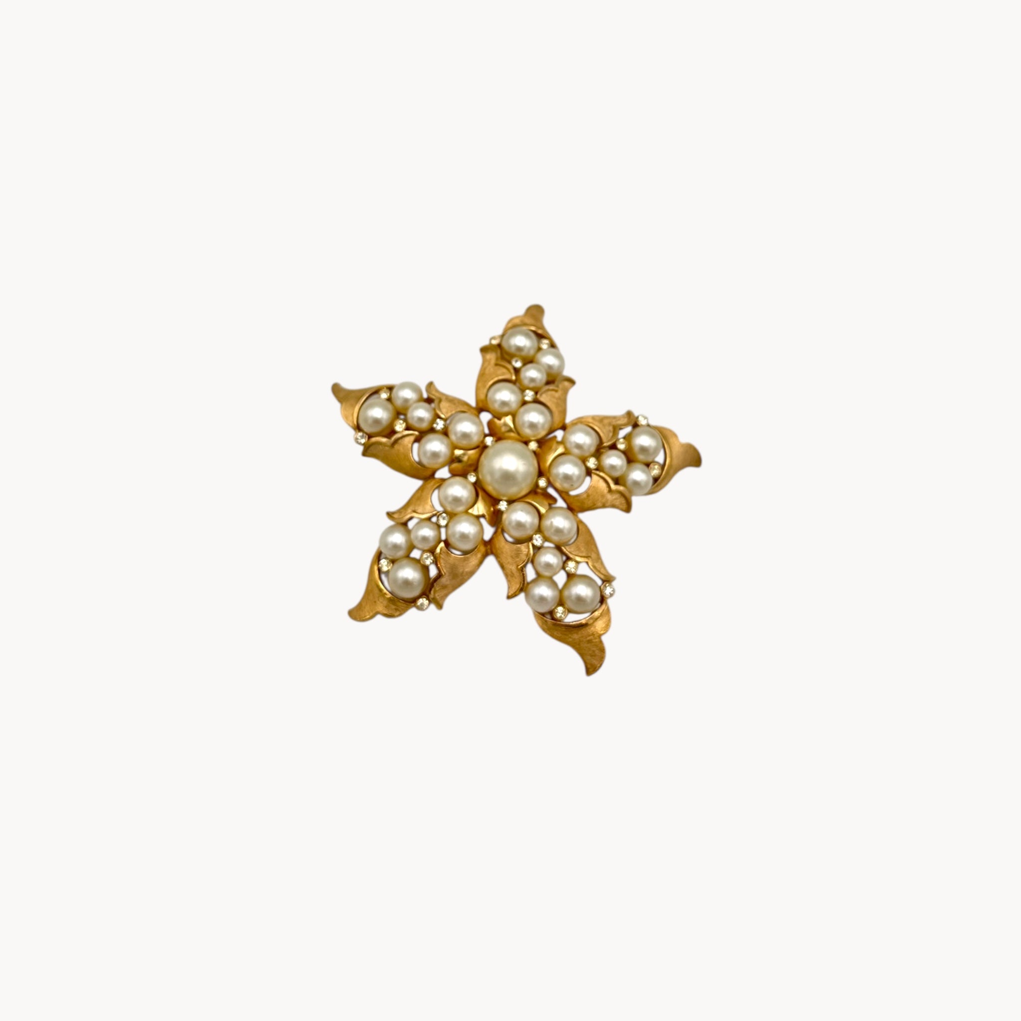 Close up view Vintage Trifari floral starfish brooch with faux pearls and rhinestones in gold-tone metal.