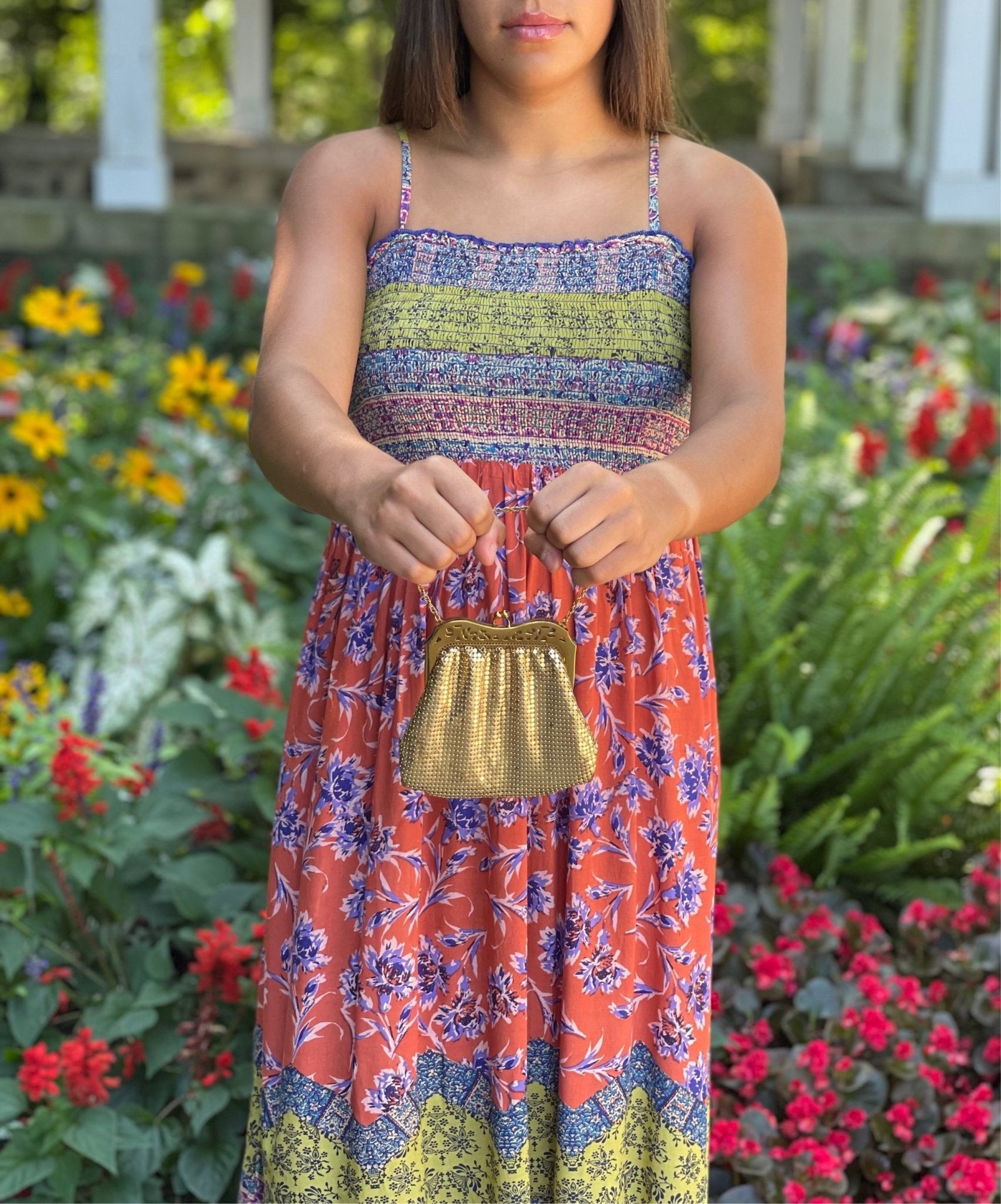 Woman holding a gold purse in front of a garden background