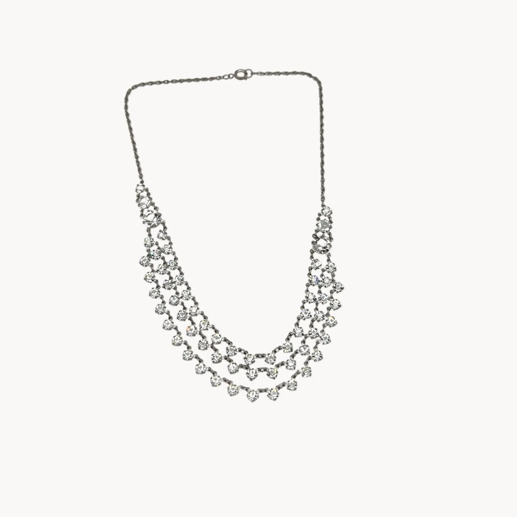 Close up view of Art Deco style rhodium plated three-row crystal draped necklace on white background.