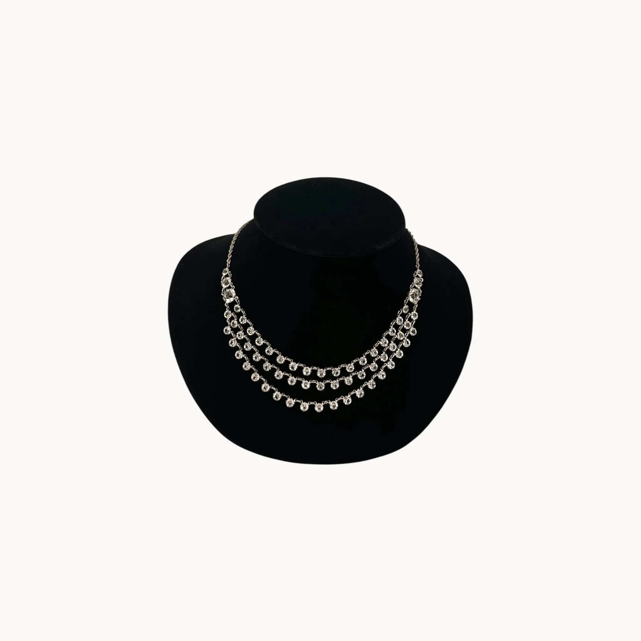Art Deco style rhodium plated three-row crystal draped necklace on black bust.