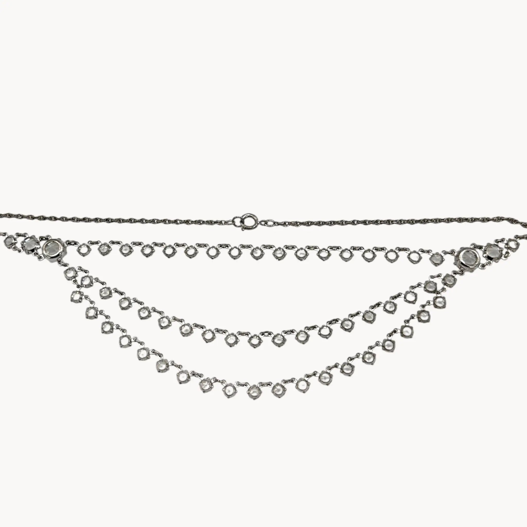 Back view of Art Deco style rhodium plated three-row crystal draped necklace on white background.