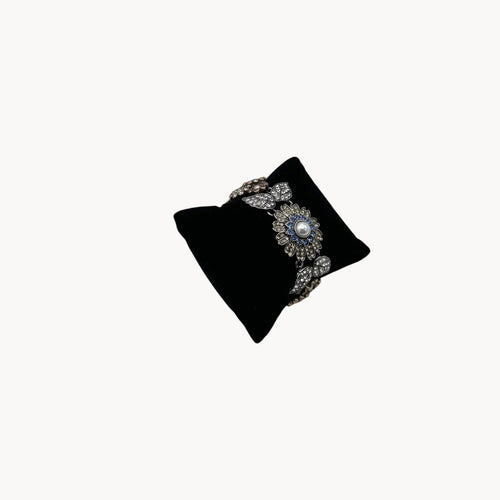 Side view of Chloe + Isabel multi-color floral rhinestone bracelet with pearls and crystal leaves on black pillow and white background. 