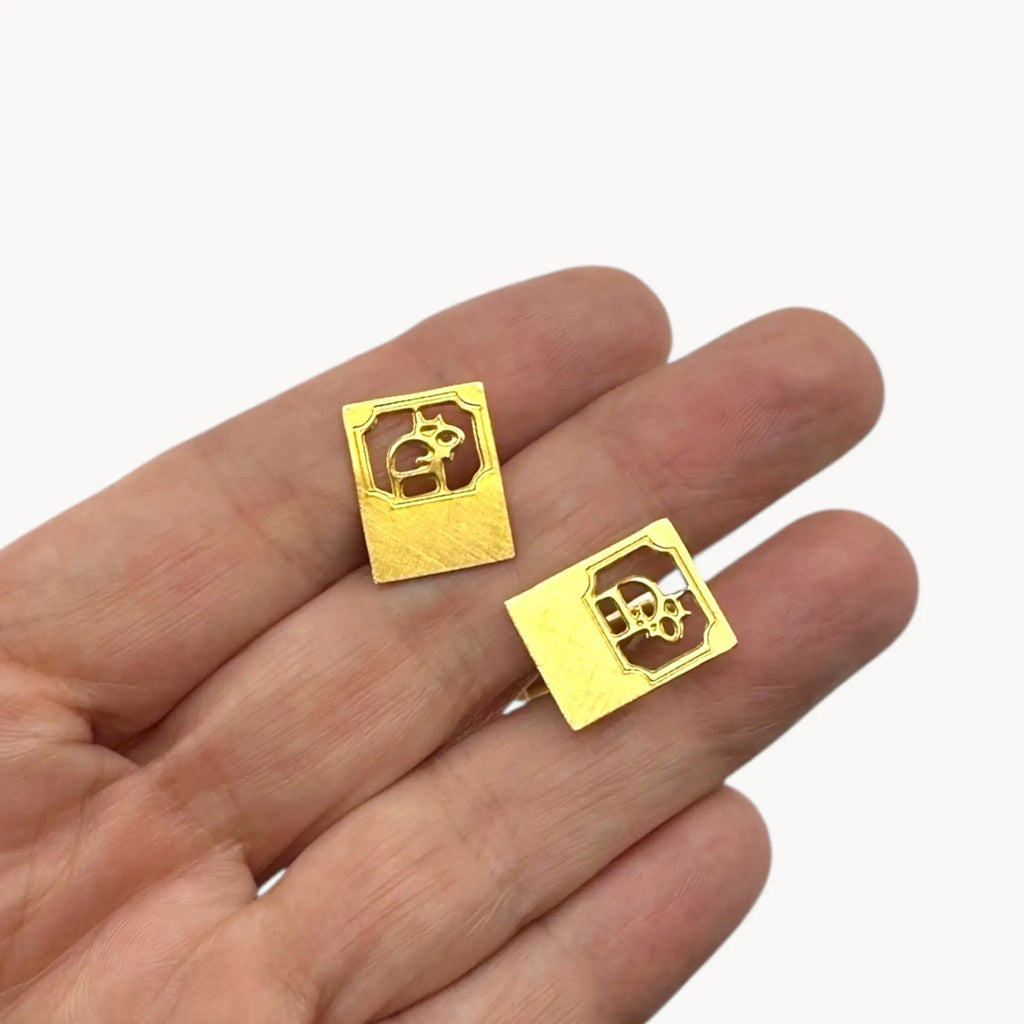 On hand to show scale, Vintage Christian Dior gold-plated square cufflinks with logo cutout design displayed on white background.