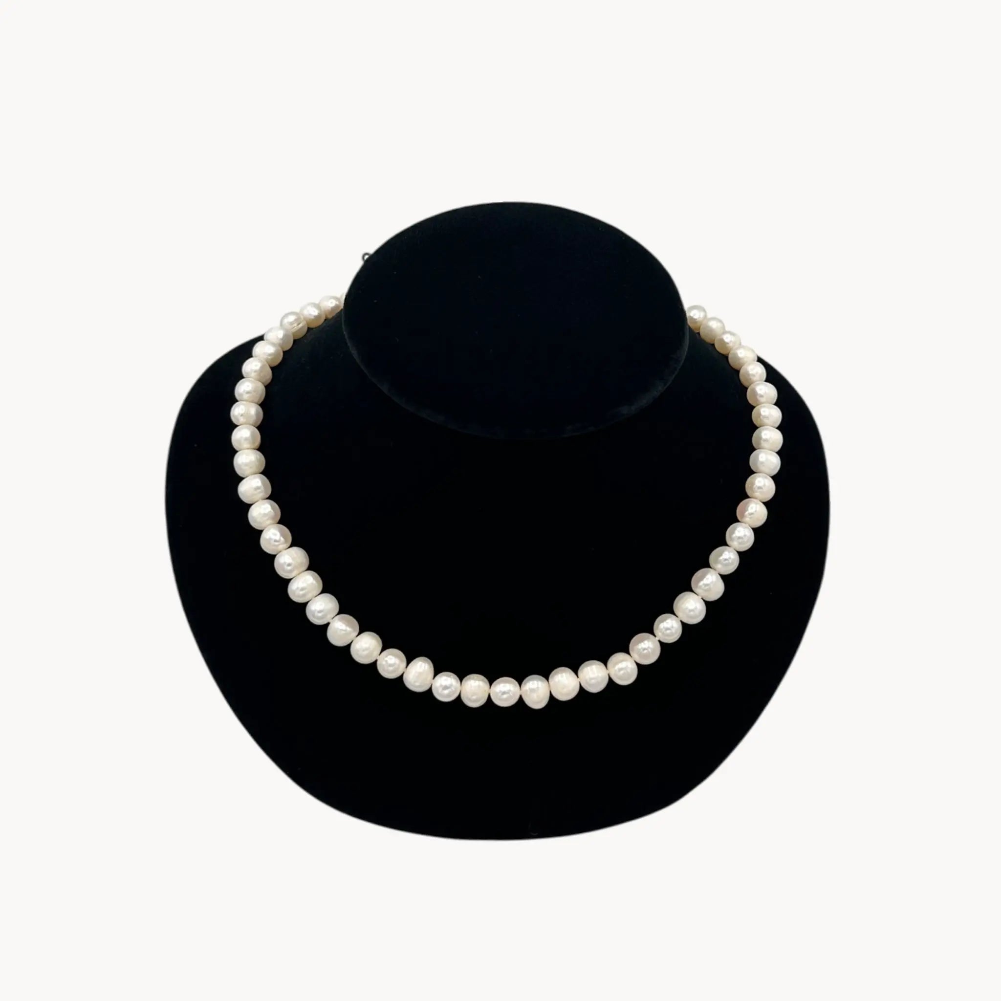 Pearl necklace on a black velvet stand against a white background