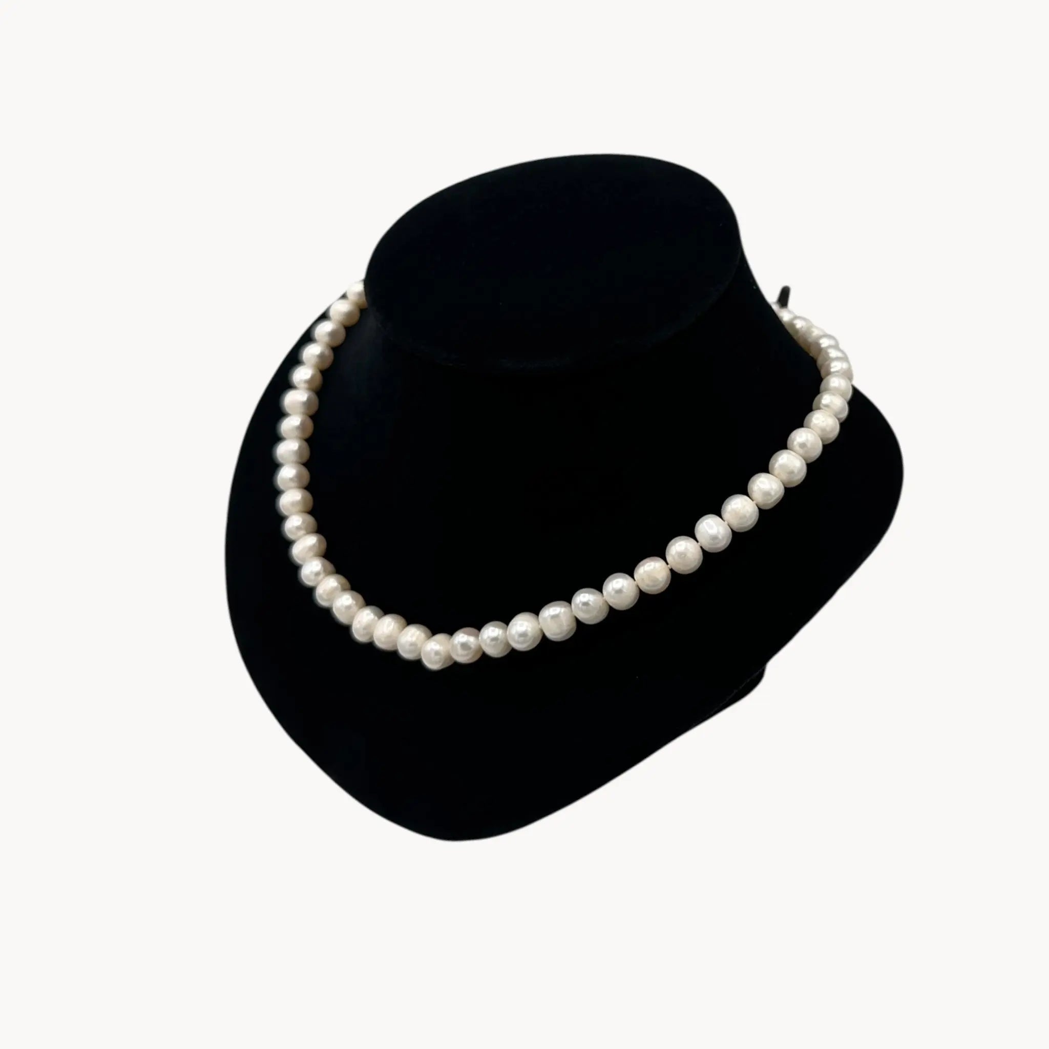 Pearl necklace on a black velvet stand against a white background