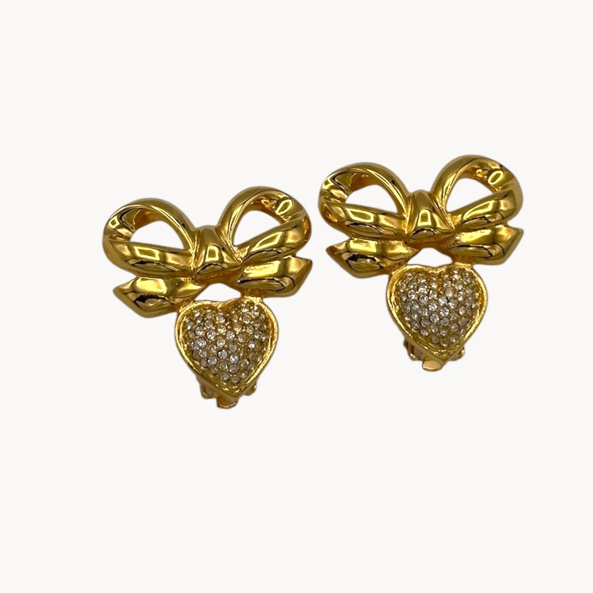 Close up view of Elizabeth Taylor gold-tone bow and pave heart earrings on white background.