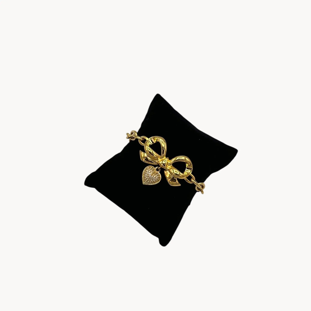 Elizabeth Taylor gold-tone bow and pave heart bracelet on black pillow.