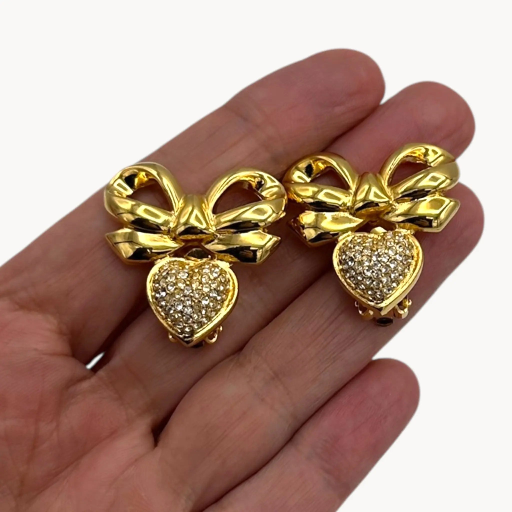 Close up view of Elizabeth Taylor gold-tone bow and pave heart earrings on hand to show scale.
