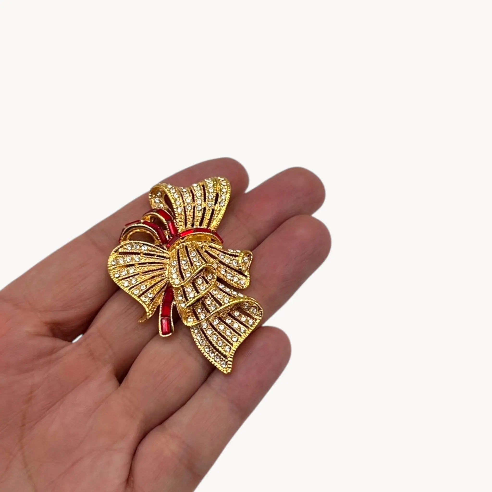 Scale size view of Jacqueline Bouvier Kennedy Camrose & Kross gold bow brooch with crystals and red rhinestones.