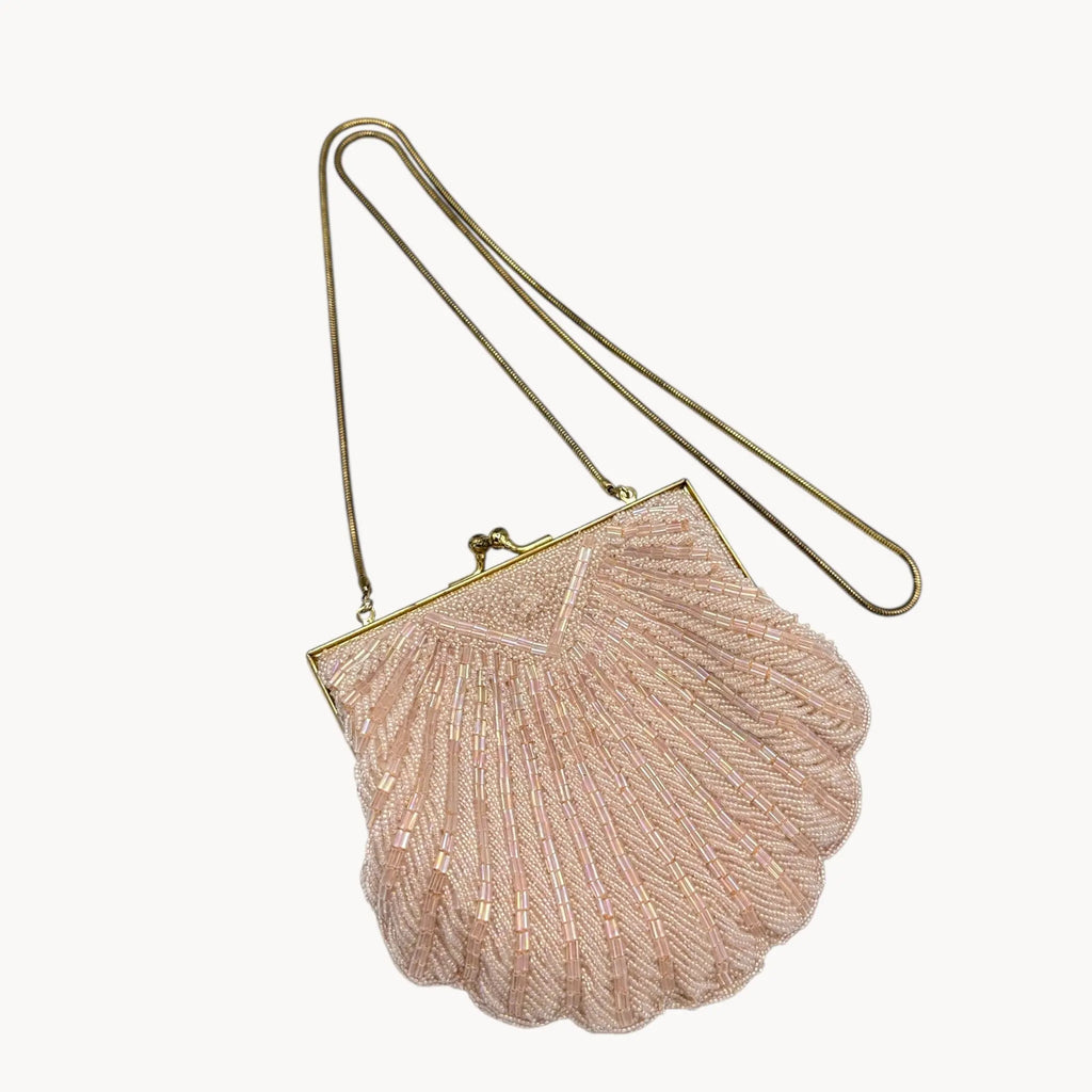 Close up view of Magid iridescent light pink beaded clamshell crossbody handbag with gold chain on white background.