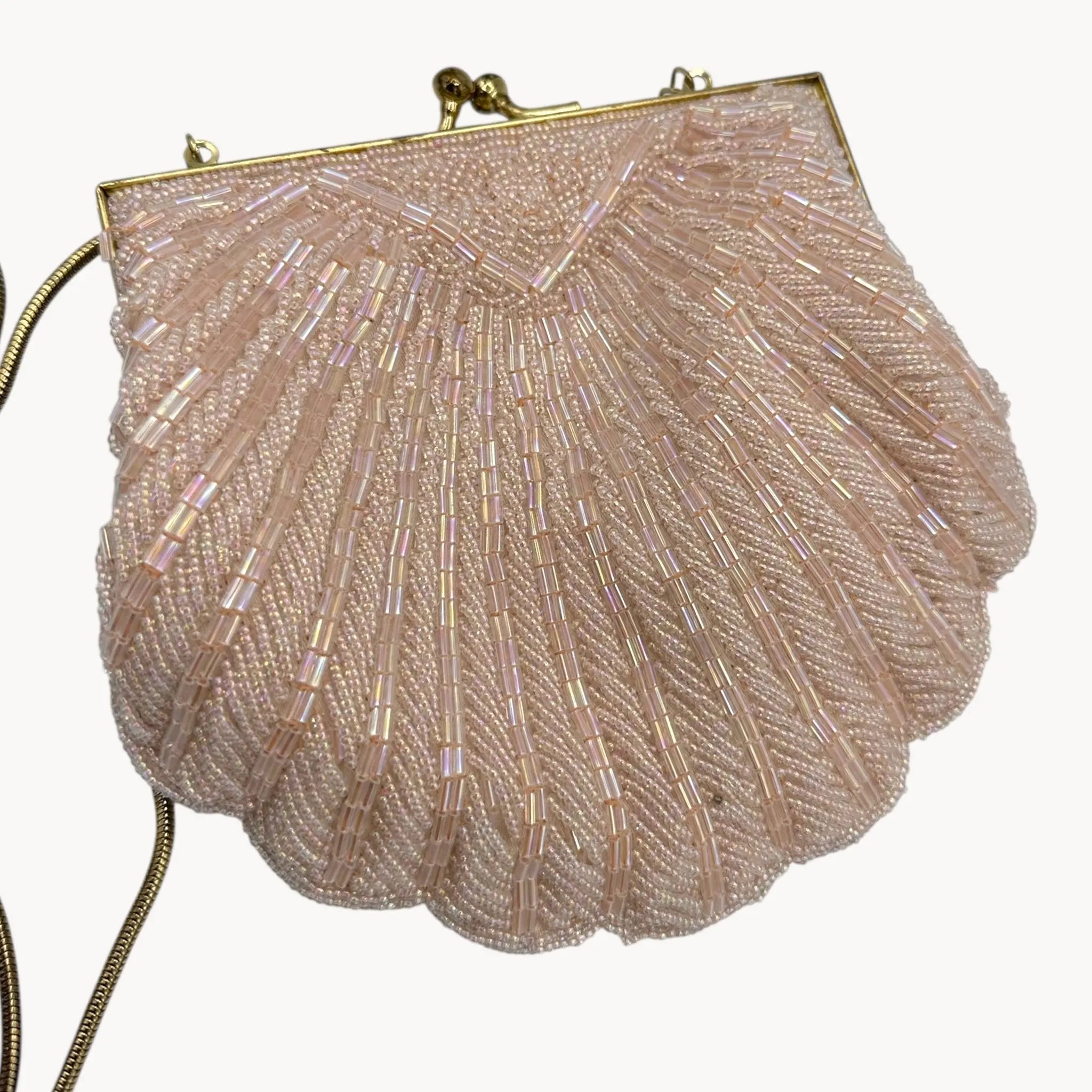 Close up of back of handbage of Magid iridescent light pink beaded clamshell crossbody handbag with gold chain on white background.