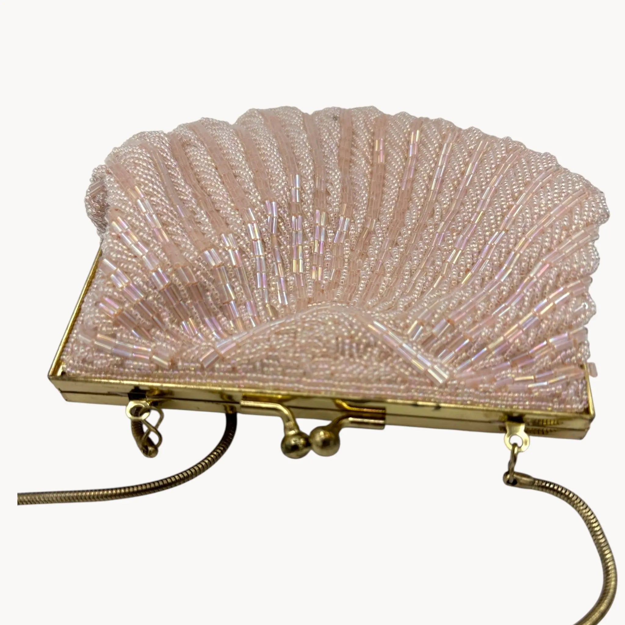 Top view of Magid iridescent light pink beaded clamshell crossbody handbag with gold chain on white background.
