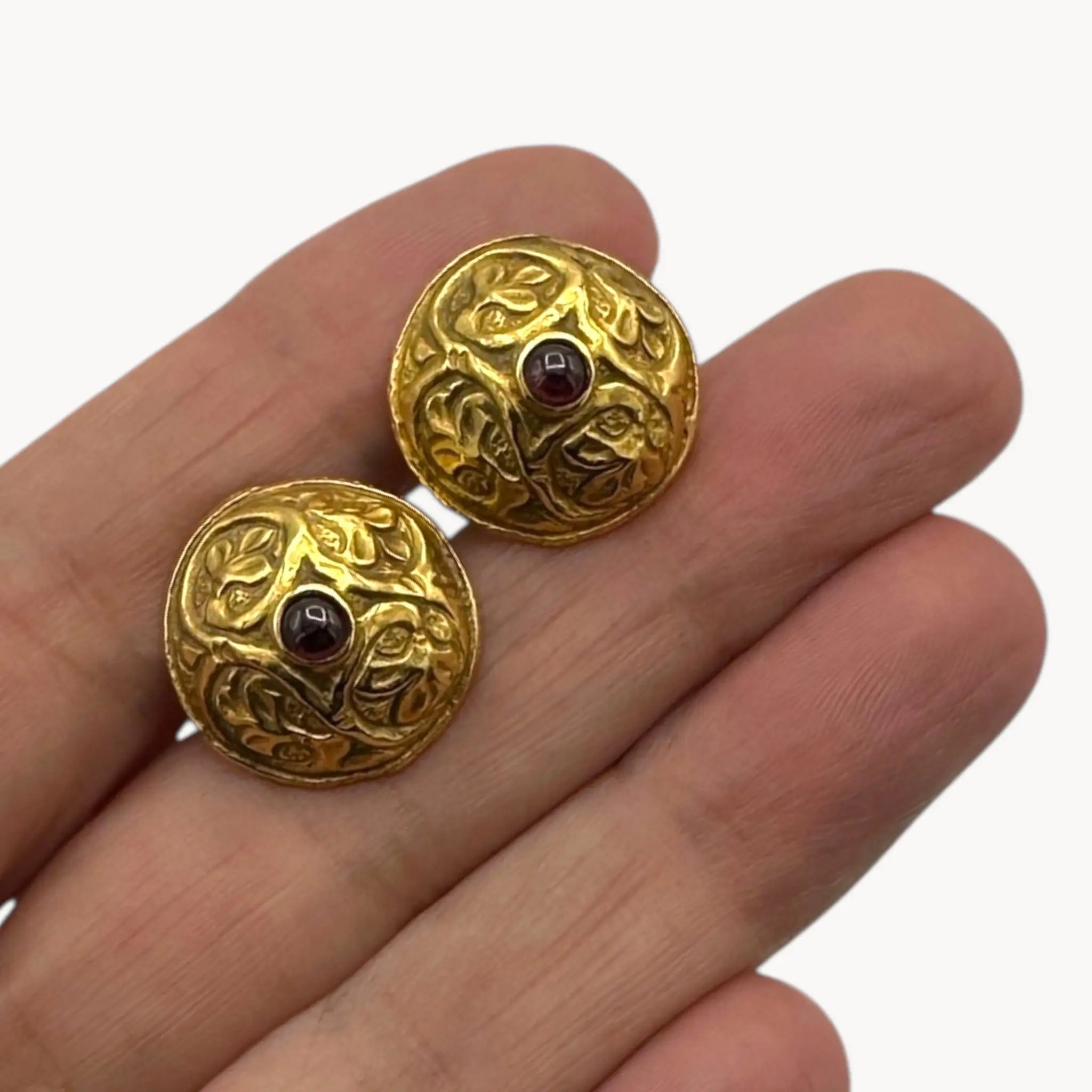 Close up displayed on hand of Vintage MMA gold embossed cufflinks with cabochon centers displayed on white background.