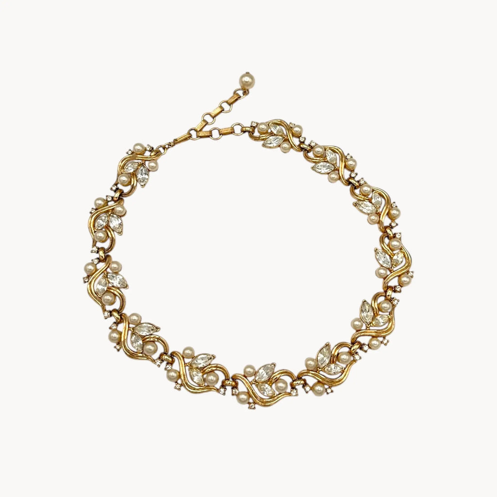 Against white background Midcentury gold floral rhinestone necklace with faux pearls.