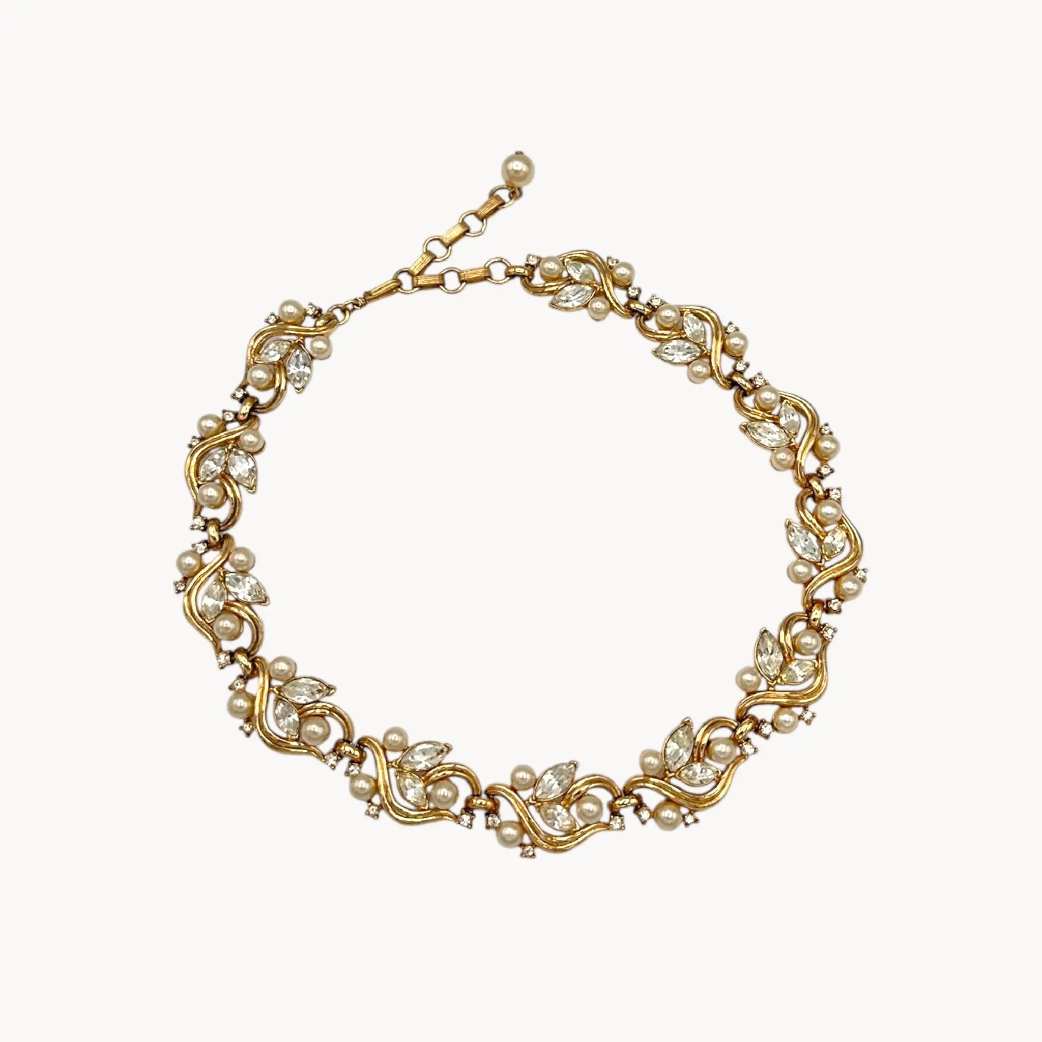 Against white background Midcentury gold floral rhinestone necklace with faux pearls.